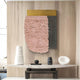 A modern entryway features a white marble console table, decorative vases, and abstract objects. Above, the Halvoria Grey & Blush Fibre Panel 3D Wall Art by Giant Sculptures adds depth with pink texture, gold accents, and a dark panel to wood-paneled walls.