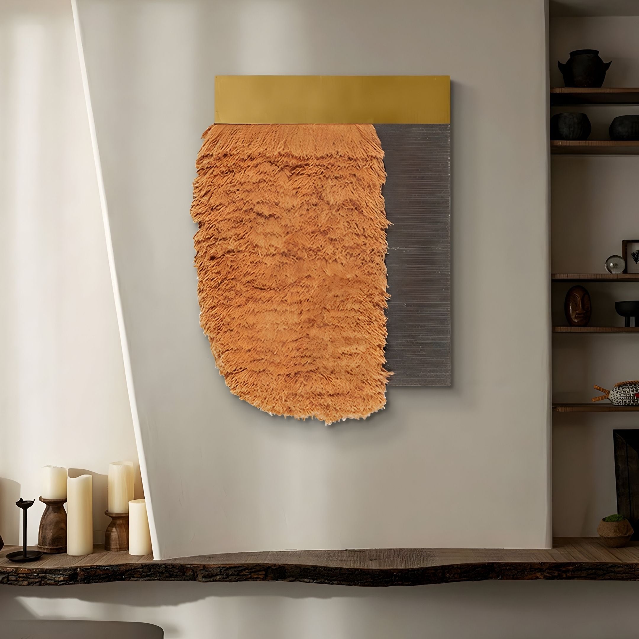 The Halvoria Grey & Terracotta Fibre Panel 3D Wall Art by Giant Sculptures features a gold top, fringed orange center, and gray panel—ideal for modern spaces. Shown above a wooden surface with candles and shelves on a neutral wall.