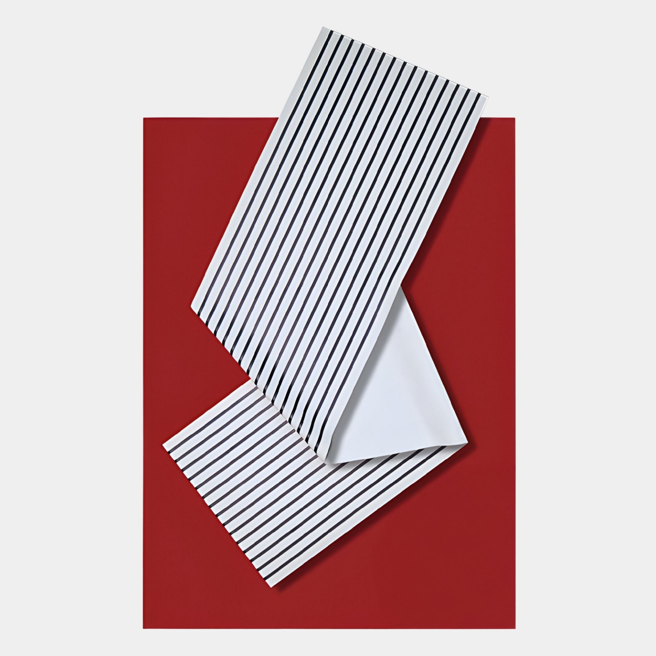 A folded white paper with black vertical stripes rests on a red rectangular background, echoing the contemporary style of Giant Sculptures' Arcluma Crimson Stripe Fold Leather 3D Wall Art in this abstract geometric composition.