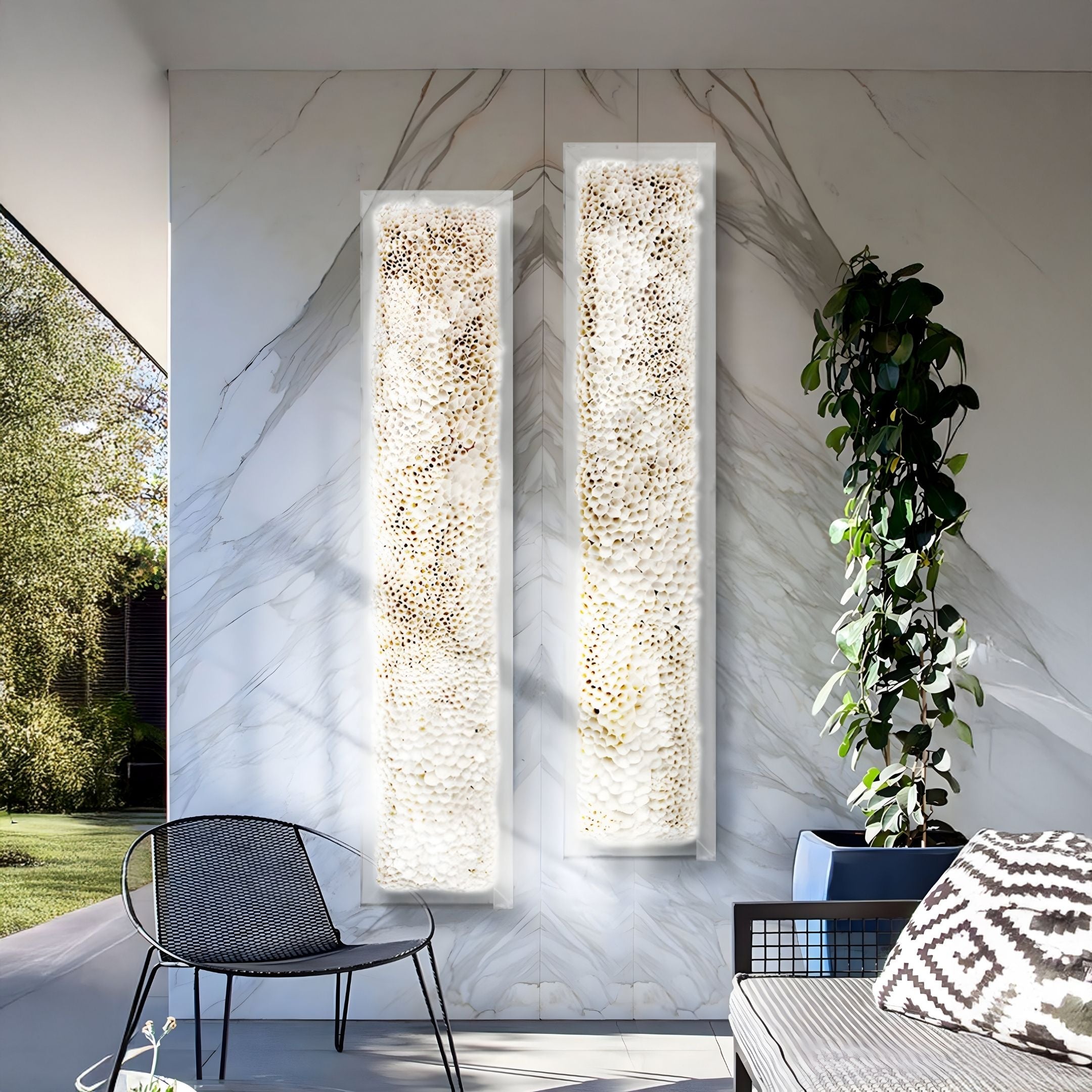 A modern patio with a marble wall showcasing Giant Sculptures' Aeraline Snowlit Ivory Vertical Gradient Leather 3D Wall Art, paired with a black mesh chair, a blue cushioned sofa with patterned pillows, and a tall green plant beside the seating area.