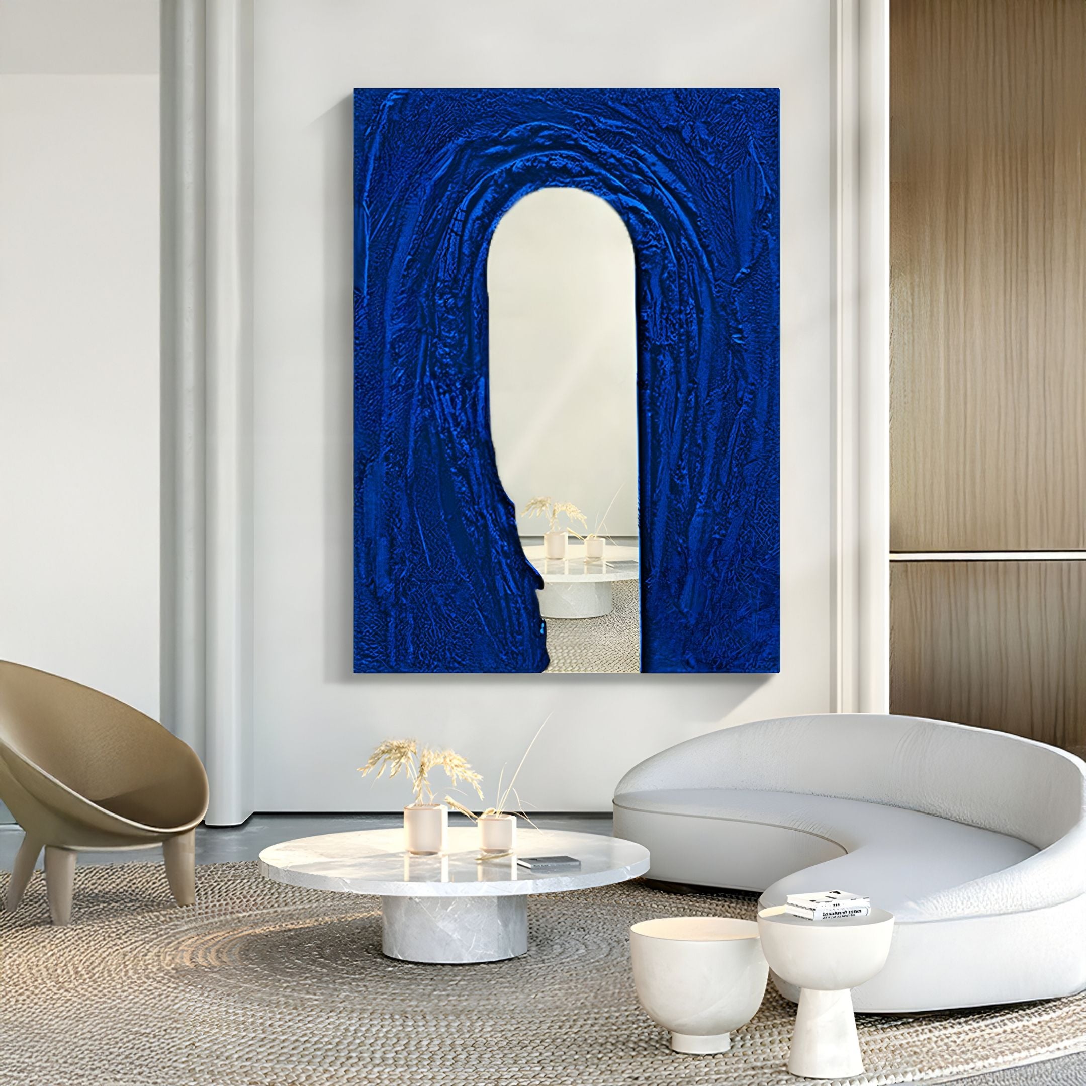 A modern living room features curved white sofas, a round marble coffee table, and the Giant Sculptures Arclunor Cobalt Blue Arch Relief Mirror 3D Wall Art. Minimal neutral decor adds calm elegance reminiscent of luxury restaurant interiors.