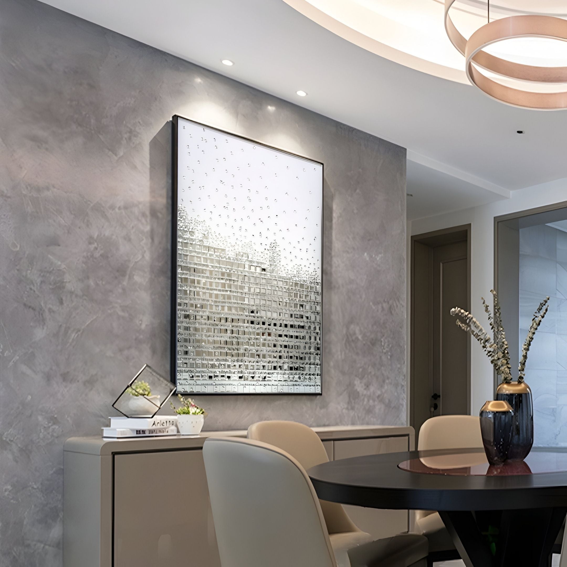 A modern dining room with beige chairs, a round dark table, abstract art, a gray textured wall, sideboard with glass decor and books, blue vase of dried flowers, and Lumicast Silver Cascade Crystal Lens 3D Wall Art by Giant Sculptures highlighted by ceiling lights.