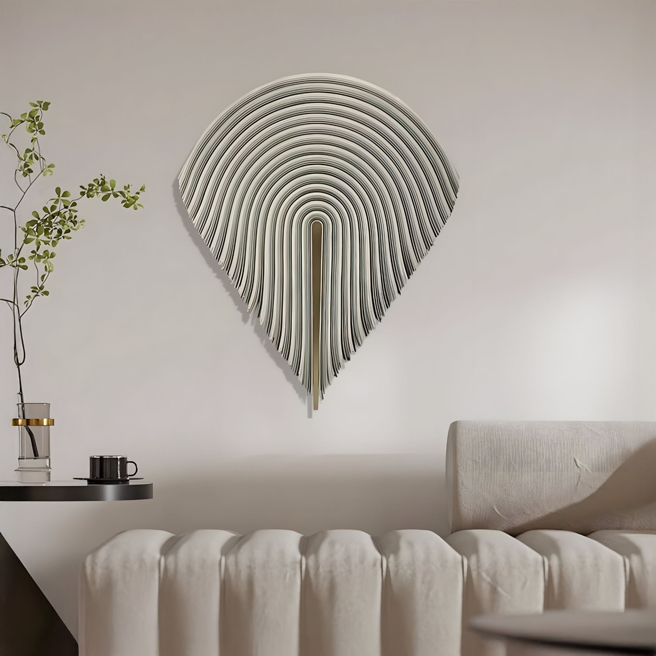 A modern living room features the Arclune Ivory Fold Sculptural Felt 3D Wall Art by Giant Sculptures with layered curves above a light sofa. Nearby, a small table with a plant, coffee cup, and books complements the wabi-sabi-inspired neutral decor.