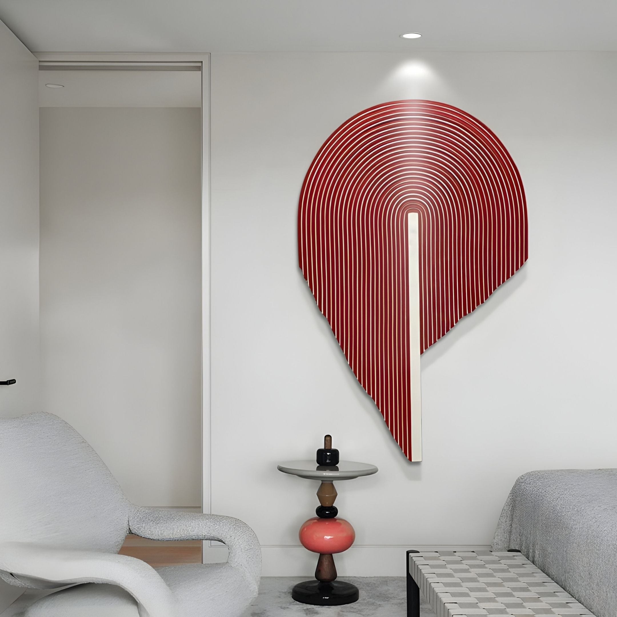 A modern, minimalist room features the Arclune Ruby Stripe Sculptural Felt 3D Wall Art by Giant Sculptures, a white armchair, a round side table with red and black accents, and a bed with a checkered bench at the foot.