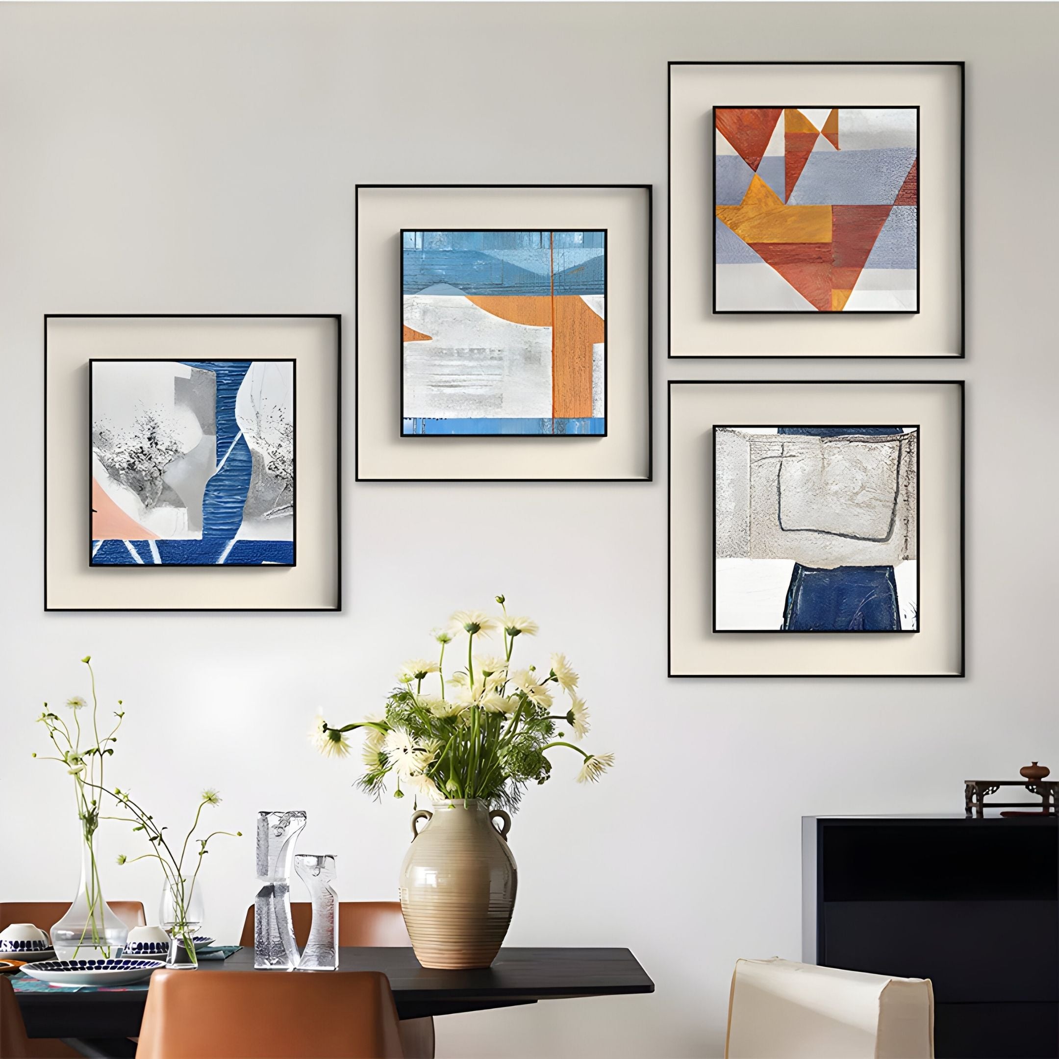 A dining area with a wooden table, brown chairs, a vase of white flowers, glassware, and four Giant Sculptures Aerolith Blue Horizon Abstract Textured Framed Wall Art pieces hanging on the wall.