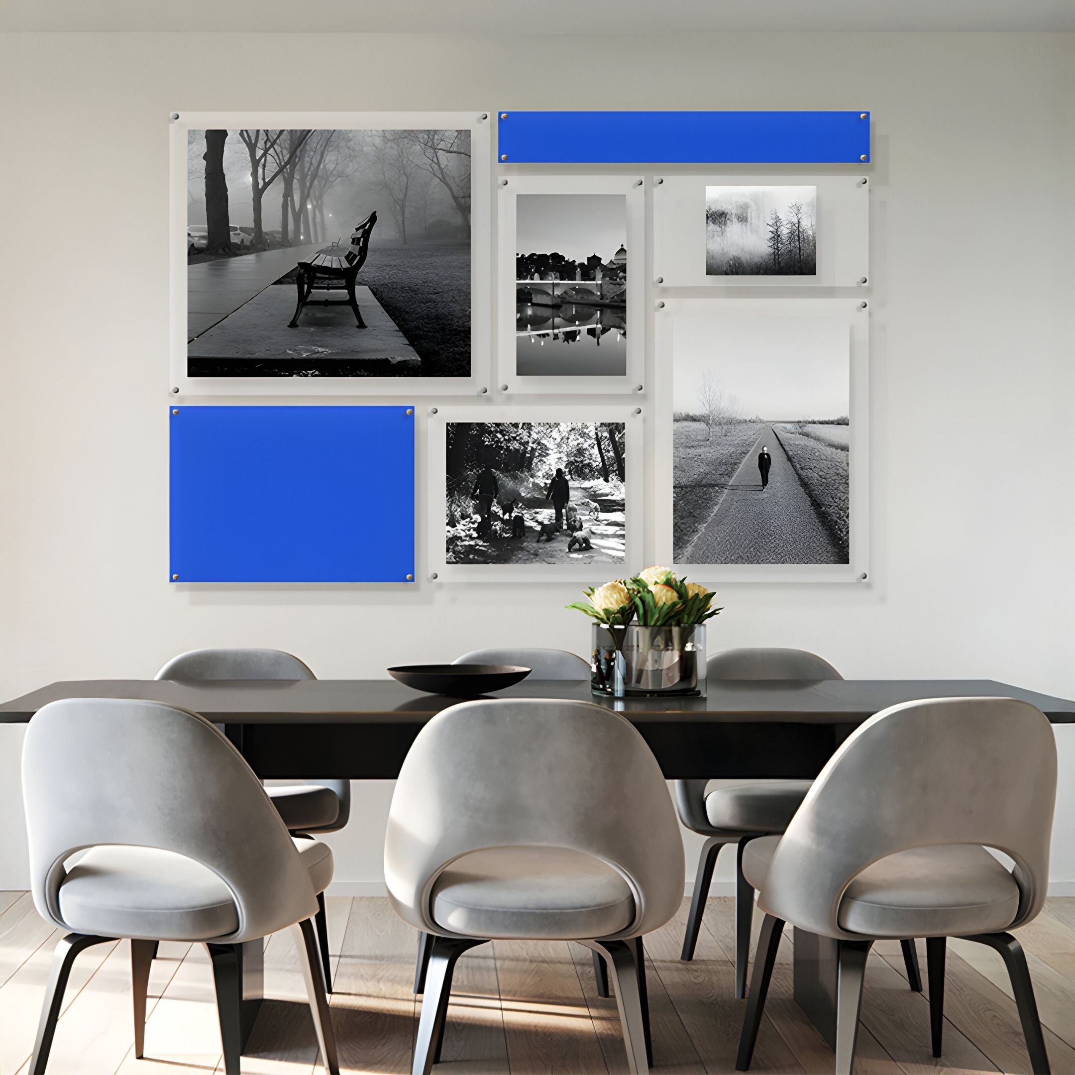 A modern dining area with a black table, gray chairs, and the "Framegrid Blue Mixed-Size Gallery 7-Set Acrylic Wall Art" by Giant Sculptures displayed in white frames. A vase with flowers brings charm to this stylish space.