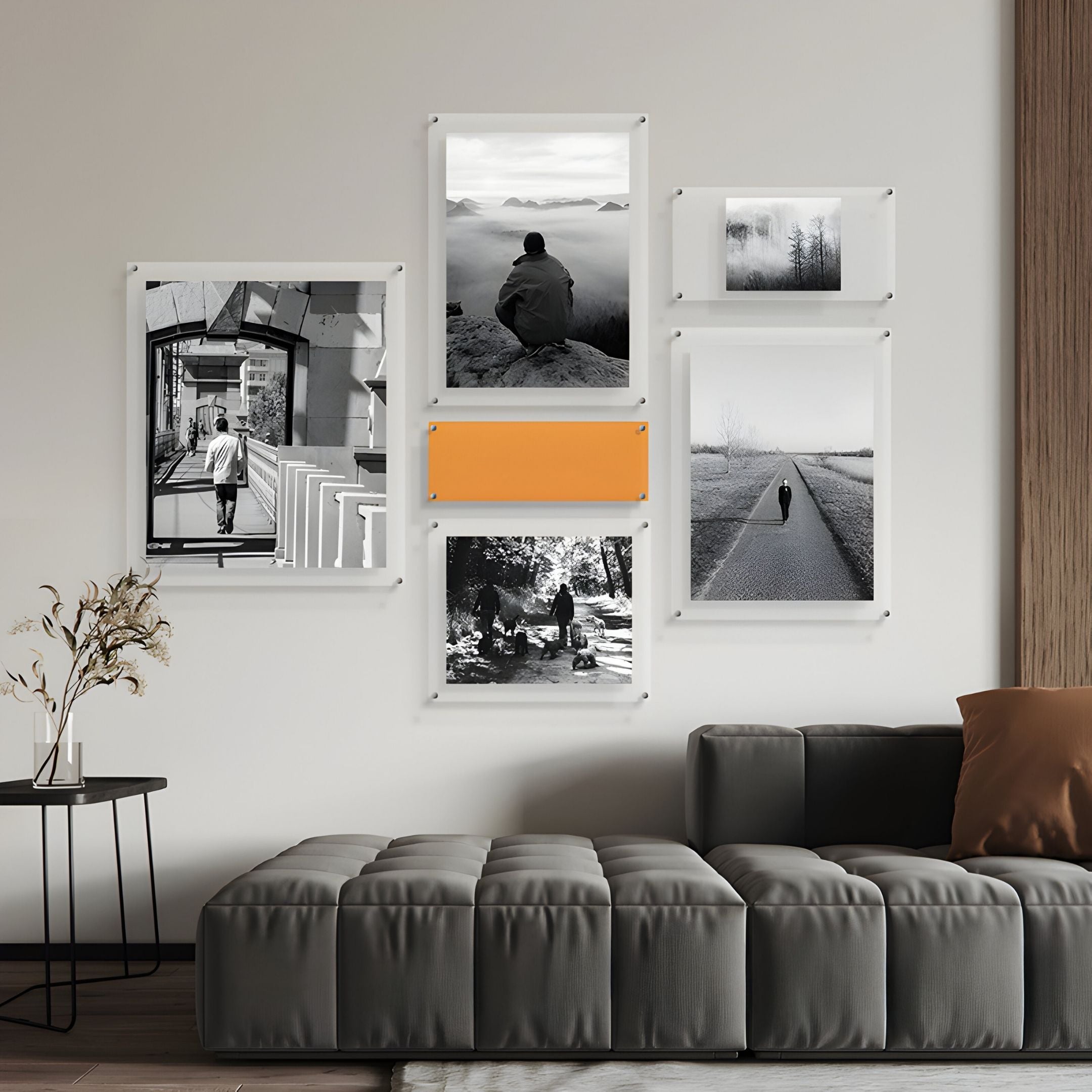 A modern living room featuring Giant Sculptures' Framegrid Orange Mixed-Size Gallery 6-Set Acrylic Wall Art—a sleek display of five black-and-white prints and one with an orange accent, all in minimalist frames—completes the stylish space.