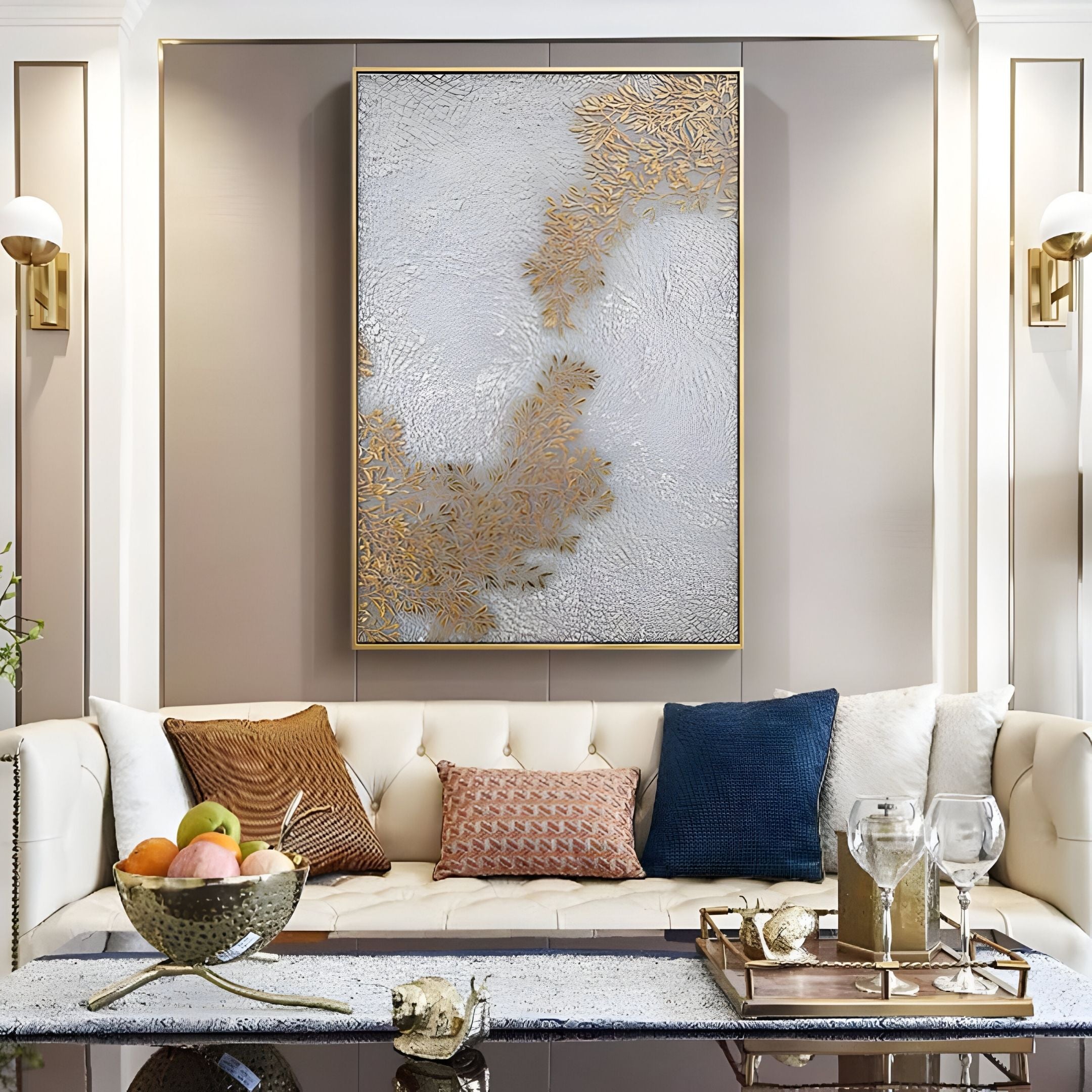 A modern living room features a cream tufted sofa, colorful throw pillows, a glass coffee table with fruit and glassware, and the Lunavine Gold Leaf Textured Silk Relief 3D Wall Art by Giant Sculptures for a luxurious touch.