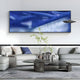 A modern living room with light gray sofas, a round black coffee table, and the Rivara Cobalt Wave Vertical Hand-Painted Rope 3D Wall Art by Giant Sculptures creates a unique focal point in this stylish interior.