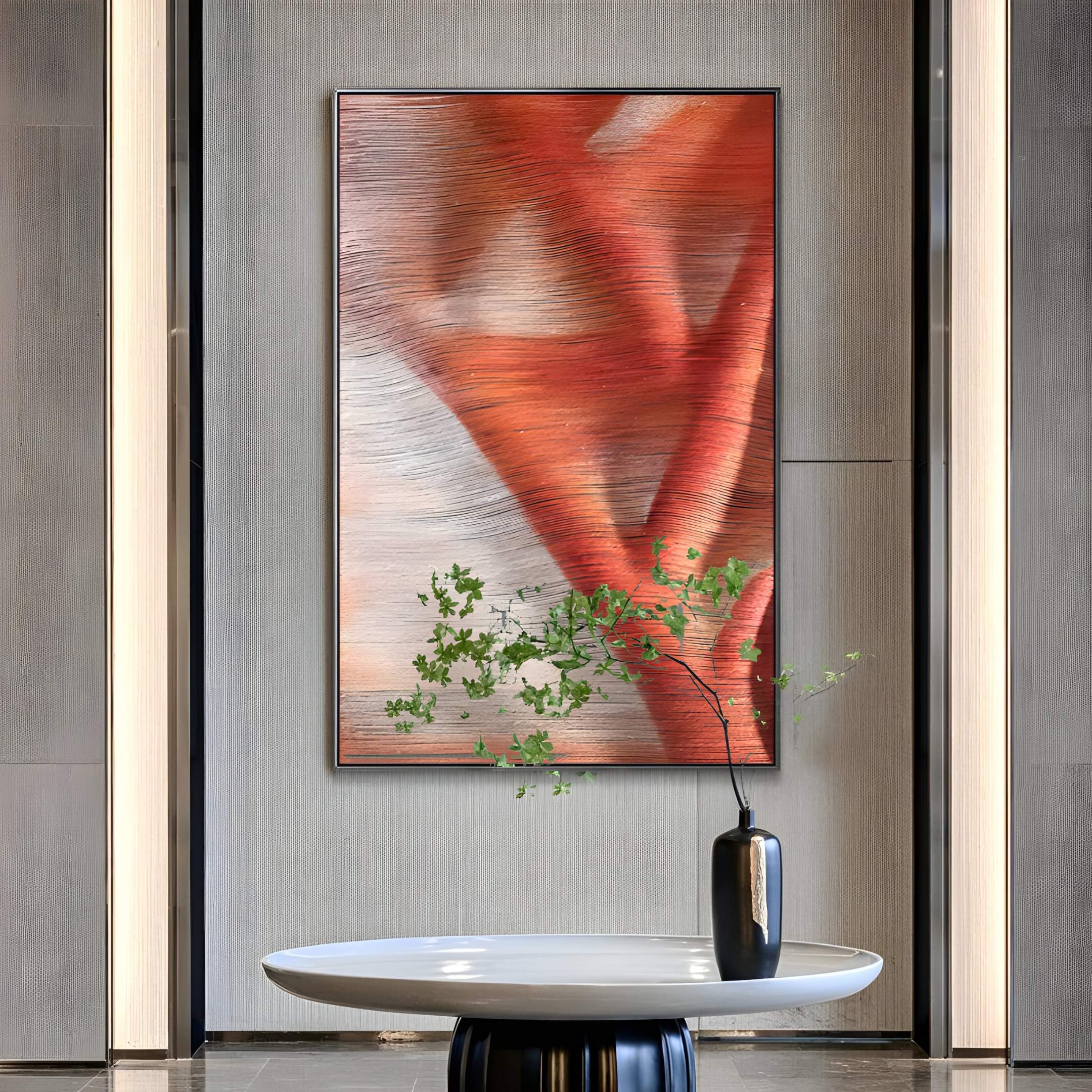 A minimal lobby features a round white table, black vase with green leaves, and the Giant Sculptures Rivara Ember Wave Hand-Painted Rope 3D Wall Art in warm red and orange on a gray wall—ideal for modern artistic interiors.