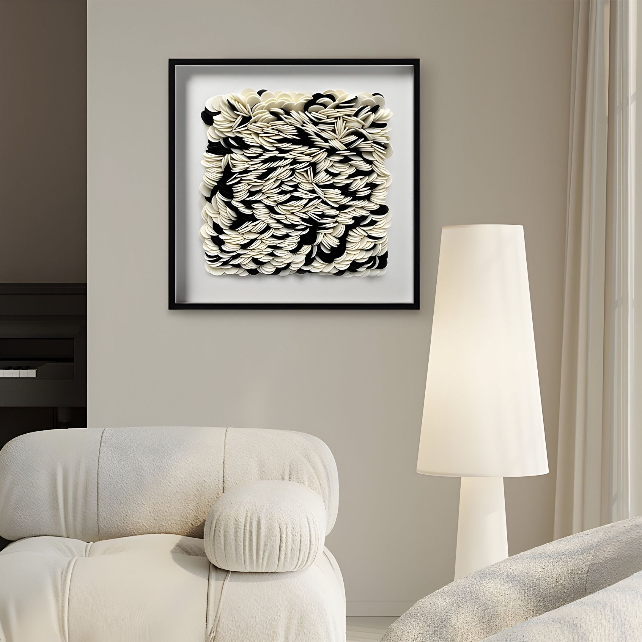 A modern living room features a white armchair, tall white floor lamp, and Giant Sculptures’ Petalus Black & Cream Layered Felt 3D Wall Art. Soft natural light through sheer curtains highlights the abstract shapes on this unique decor piece.