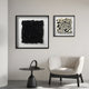 A modern minimalist room with a white armchair, small black side table, and striking Petalus Black Layered Felt 3D Wall Art by Giant Sculptures hanging on a light gray wall.