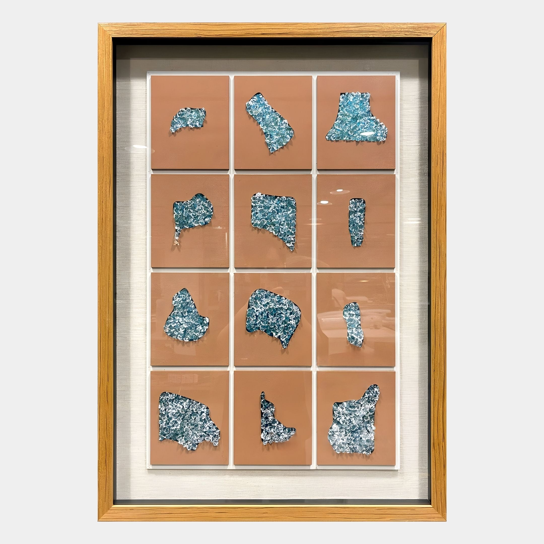 The Agliera Aqua Crystal Shard Grid Framed 3D Wall Art by Giant Sculptures features 12 shiny, silver-blue abstract relief tiles on nude-pink squares, set in a beige background and wooden frame in a modern 3x4 grid design.