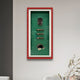 The Cavendor Cigar & Badge Green Framed Wall Art by Giant Sculptures features three cigars, a lighter, cutter, and ashtray on a green background with a red border. A plant sits in the lower right corner against a gray wall.