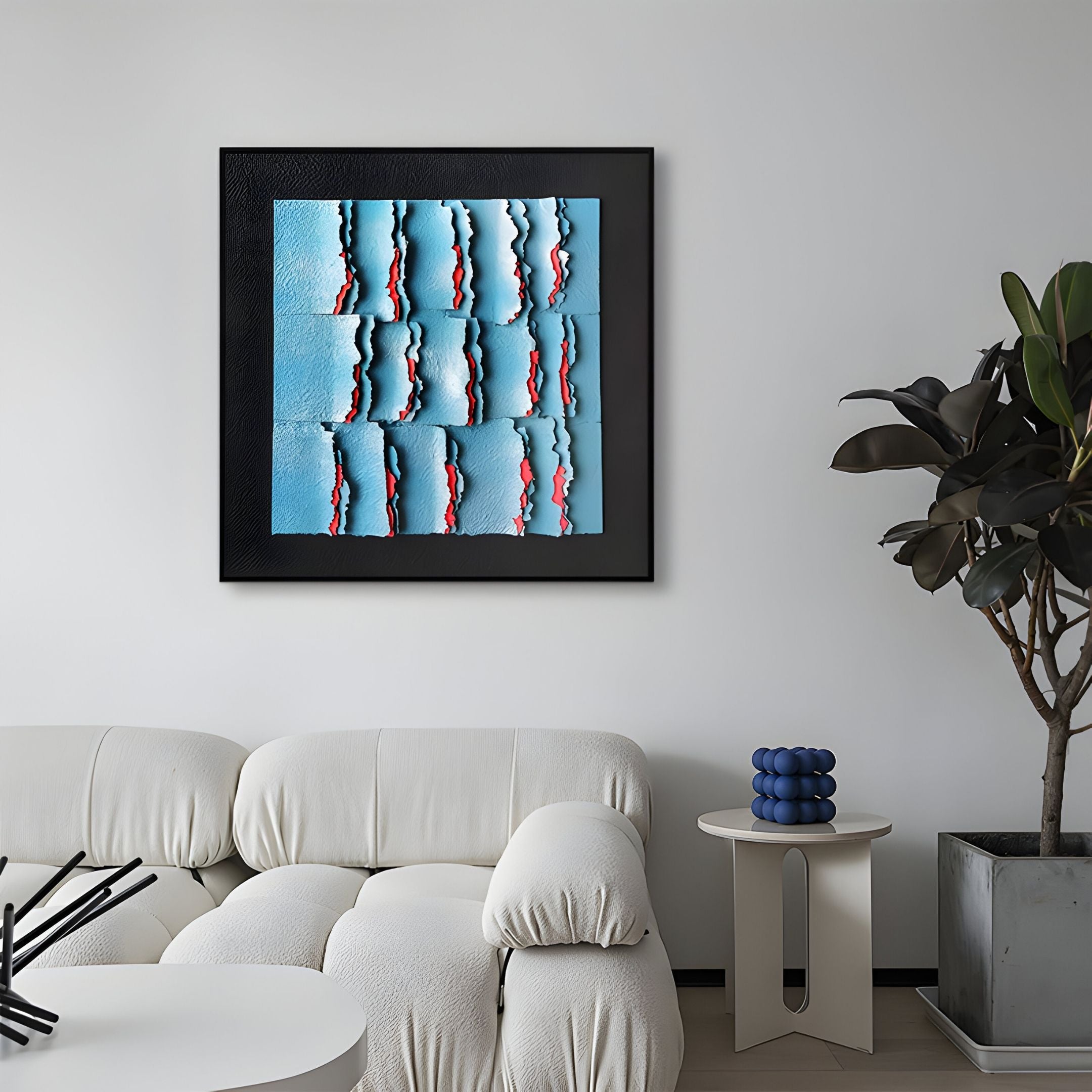 A modern living room with a white sofa, a small round side table, a potted plant, and the Rivura Blue Layered Sandstone Texture 3D Wall Art by Giant Sculptures in a sleek black frame displayed on the wall.