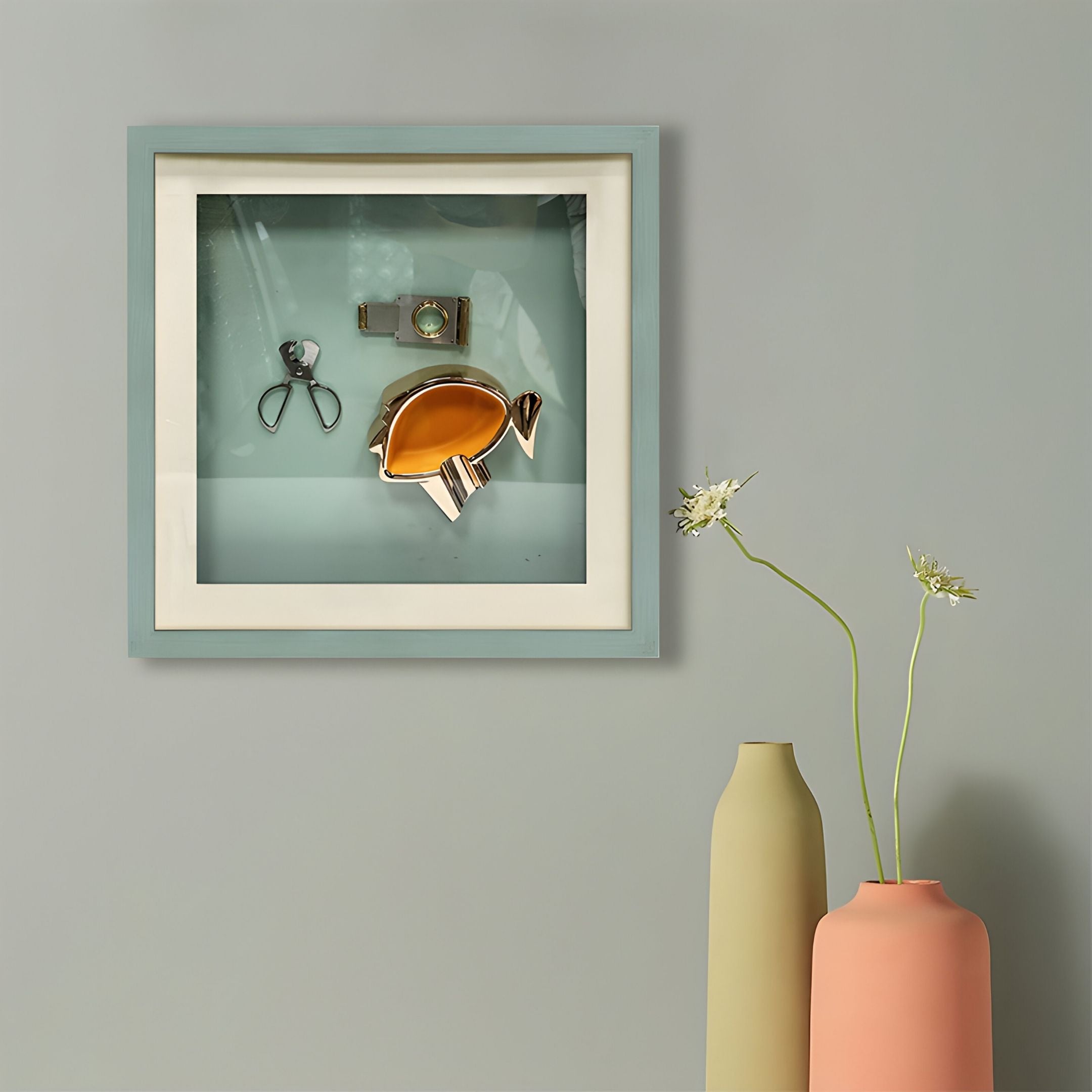 The Giant Sculptures Cavallero Aqua Cigar Tools & Metal Ashtray Framed Wall Art hangs on a gray wall above two tall vases, creating an intriguing sculptural accent with delicate flowers.