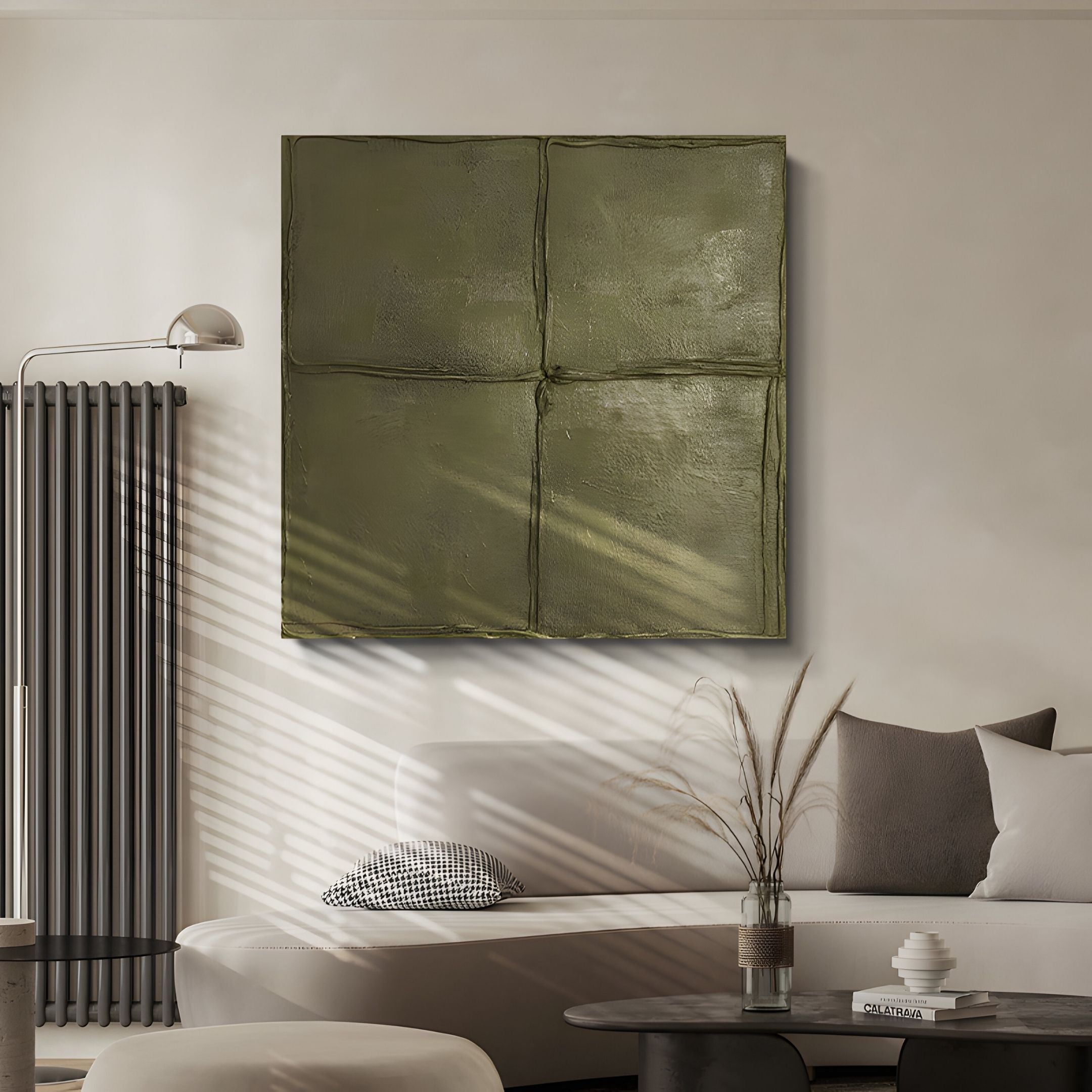 A modern living room features a neutral sofa, cushions, and a round coffee table with a vase of dried grass. Above, Giant Sculptures' Terracrecta Olive Painted Textured Square 3D Wall Art stands out, softly lit by natural light through the blinds.