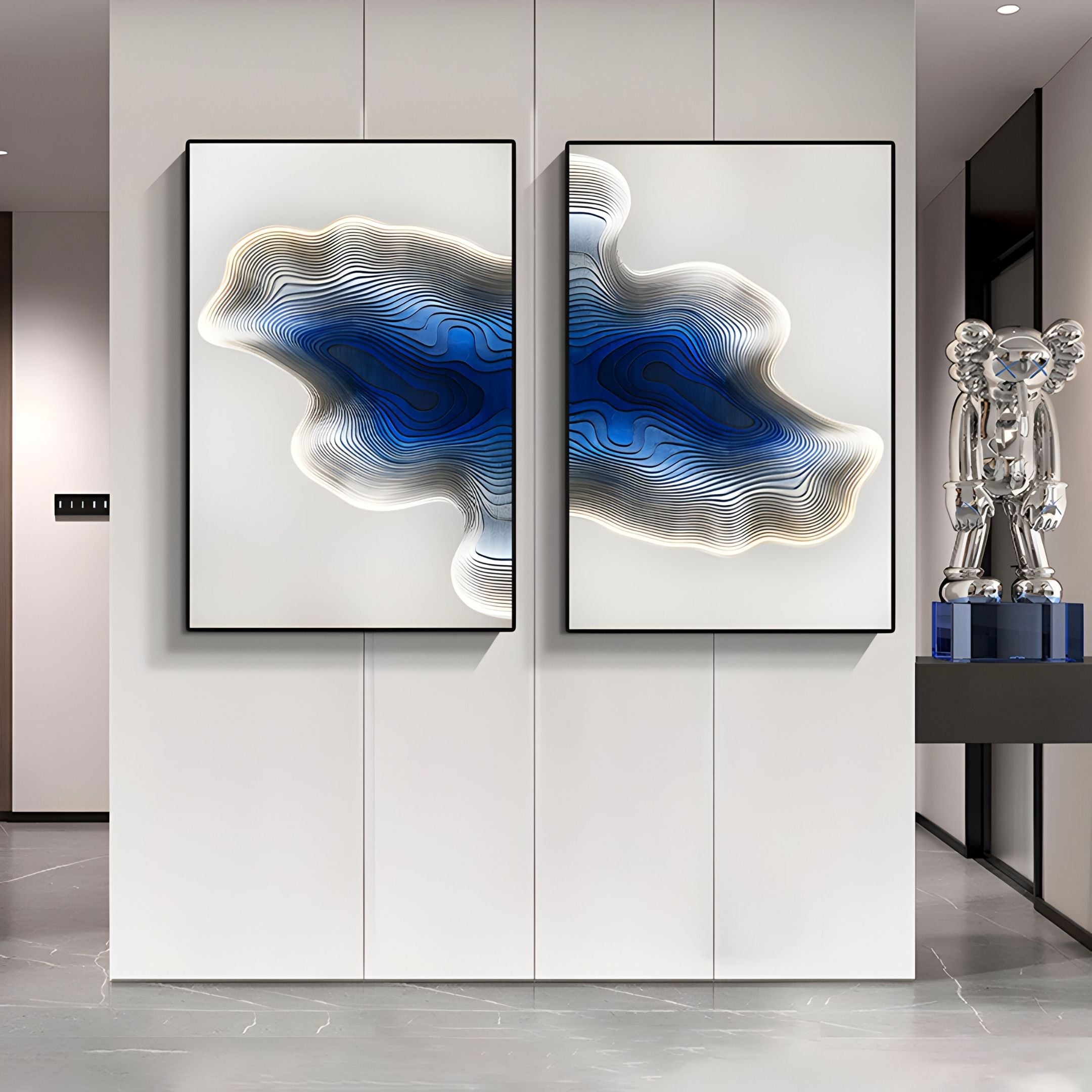 Two Stratona Blue Contour Layered Wood Relief 3D Wall Art pieces by Giant Sculptures hang side by side on a white wall. To the right, a shiny silver bear sculpture is displayed on a blue pedestal.
