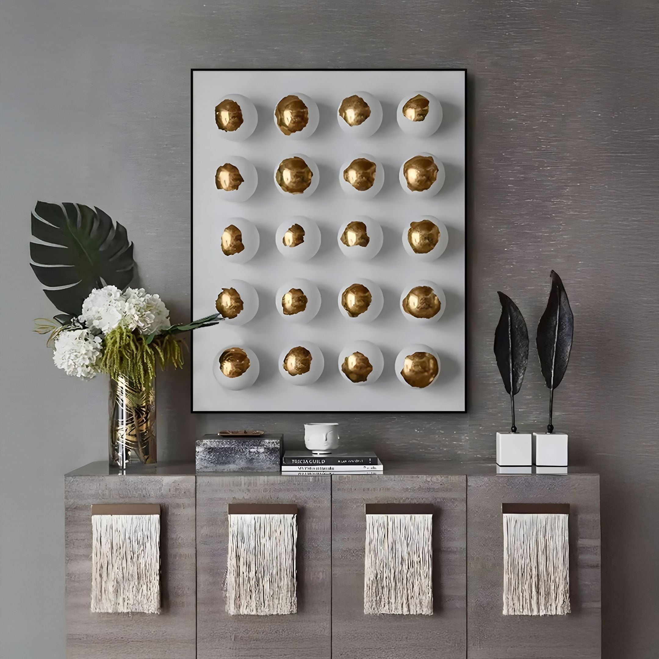 A modern console table with textured panels displays a vase of white flowers, books, and accents. Above it hangs Giant Sculptures' Orbivelle Gold Patch Sphere & White Panel 3D Wall Art, bringing a striking contemporary touch to the space.