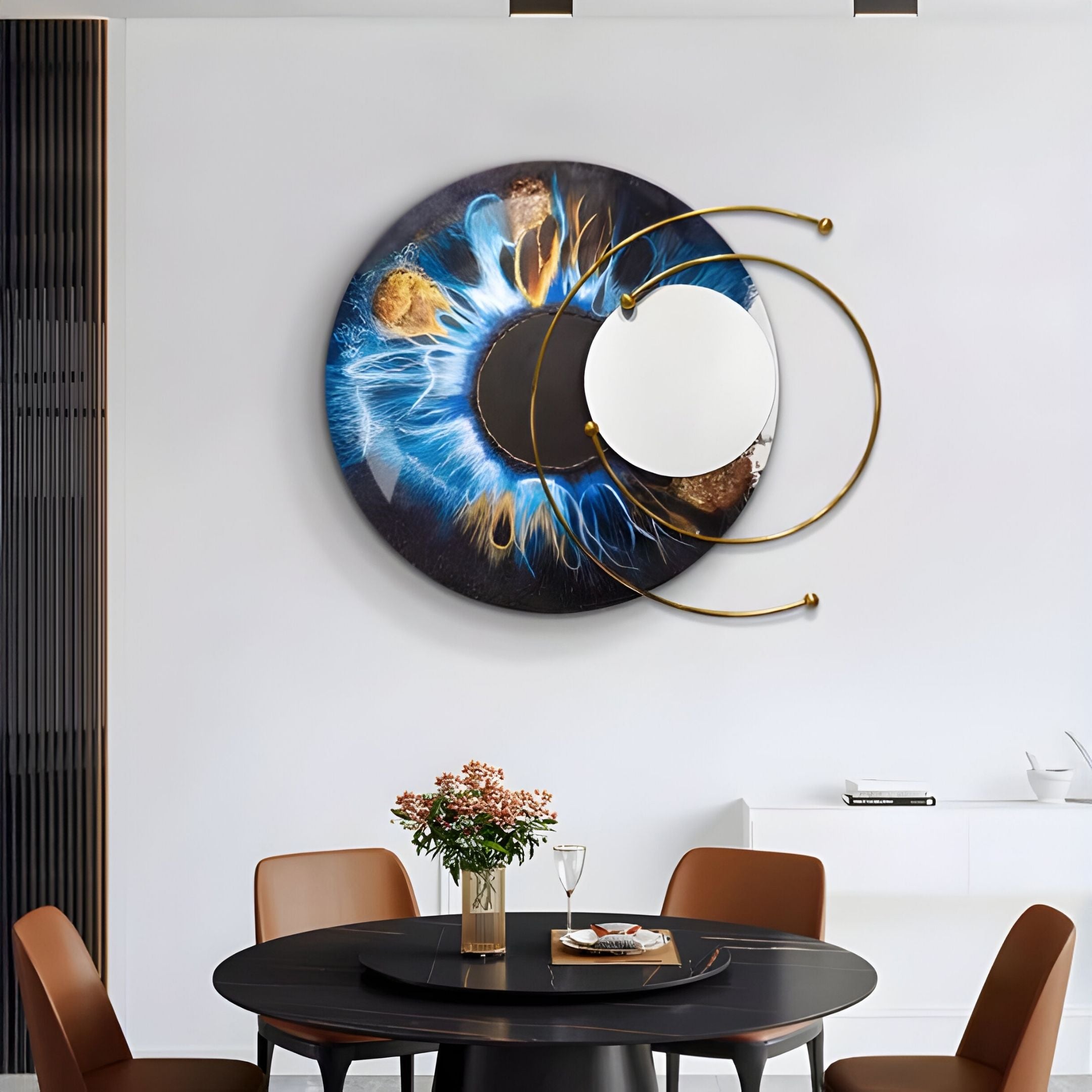A modern dining area with a round black table, brown chairs, and pink flowers. Above, the white wall is adorned with Giant Sculptures' Aurelios Cosmic Blue Crystal Porcelain & Gold Orbit 3D Wall Art for an artistic touch.