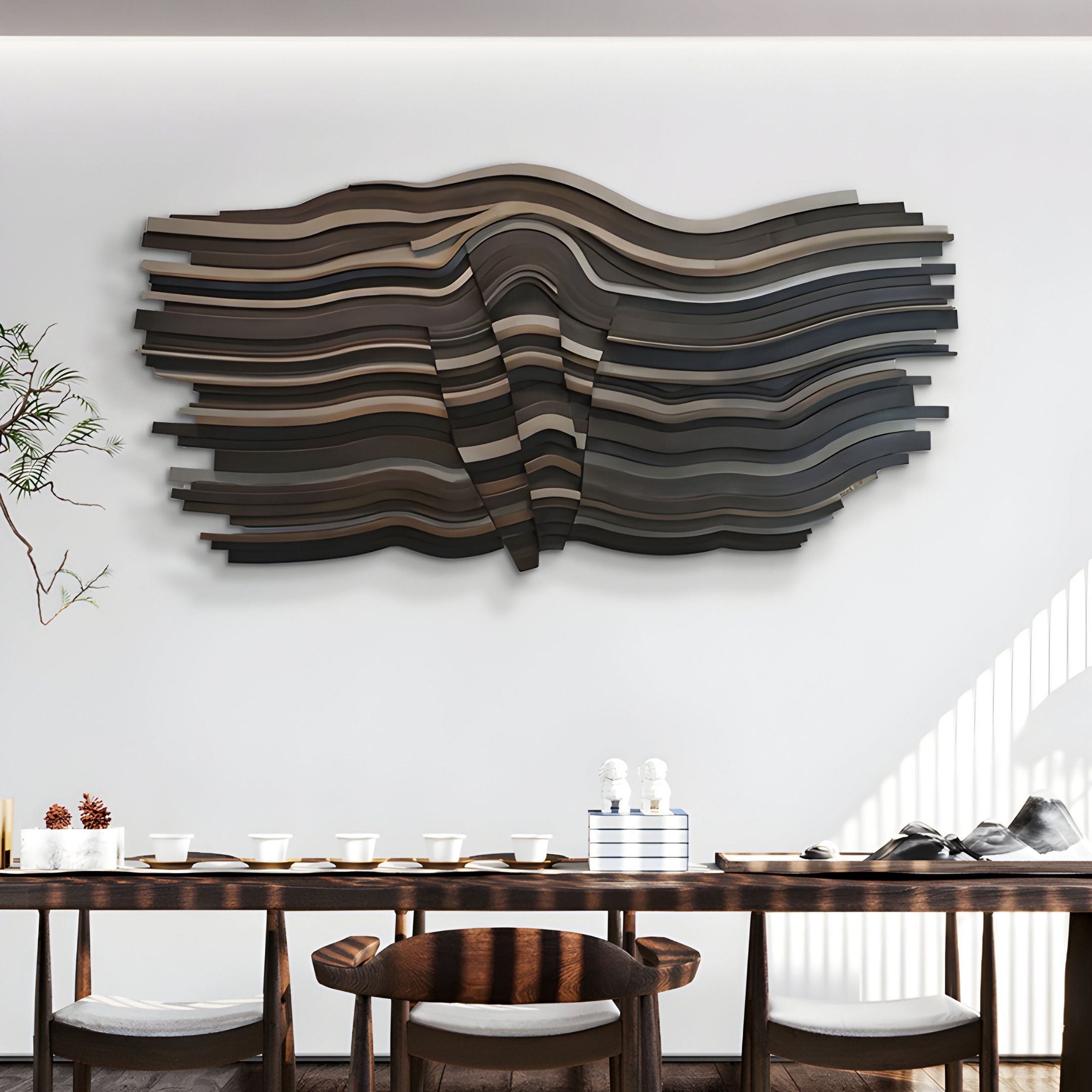 A modern dining room features a long wooden table set with white dishes. Above it hangs the Stratava Driftwave Layered Wood Carving 3D Wall Art by Giant Sculptures in black, brown, and gray, casting dramatic shadows on the white wall.