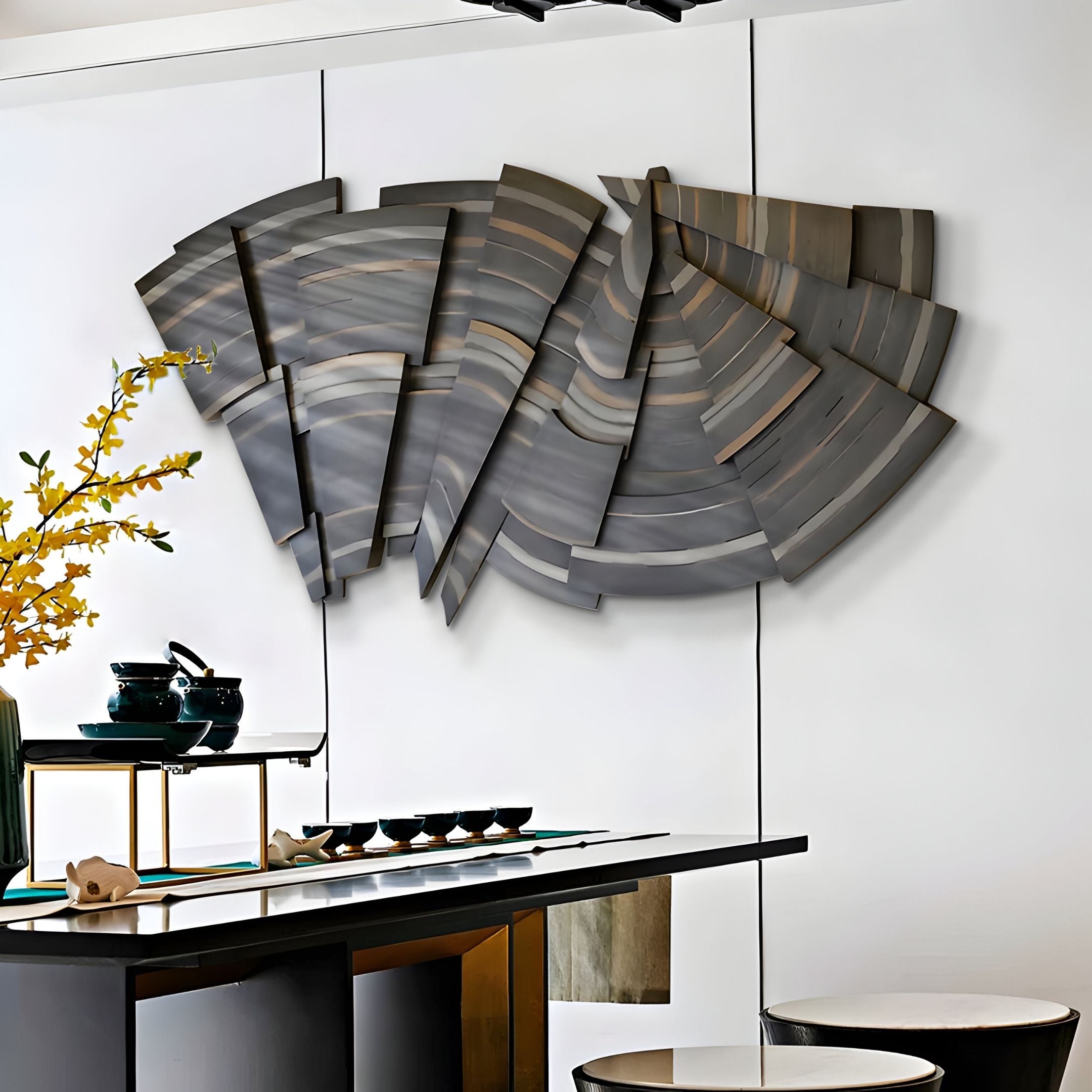 A modern dining area features the Stratava Arcstone Layered Wood Carving 3D Wall Art by Giant Sculptures, a table set with black teapots and cups, yellow flowers in a vase, two white stools, and minimalist, elegant décor.