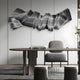A modern office with a sleek desk, gray upholstered chair, and the Vellun Wave Charcoal Grey Sculptural 3D Wall Art by Giant Sculptures on a light-paneled wall. Minimalist decor features books, a plant, and a patterned rug for effortless style.
