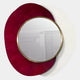 The Solistra Crimson II Layered Round Mirror 3D Wall Art by Giant Sculptures features a gold-framed round mirror on overlapping red and white backplates, forming bold wall decor. Its reflection shows a gray cabinet and potted plant against a light backdrop.