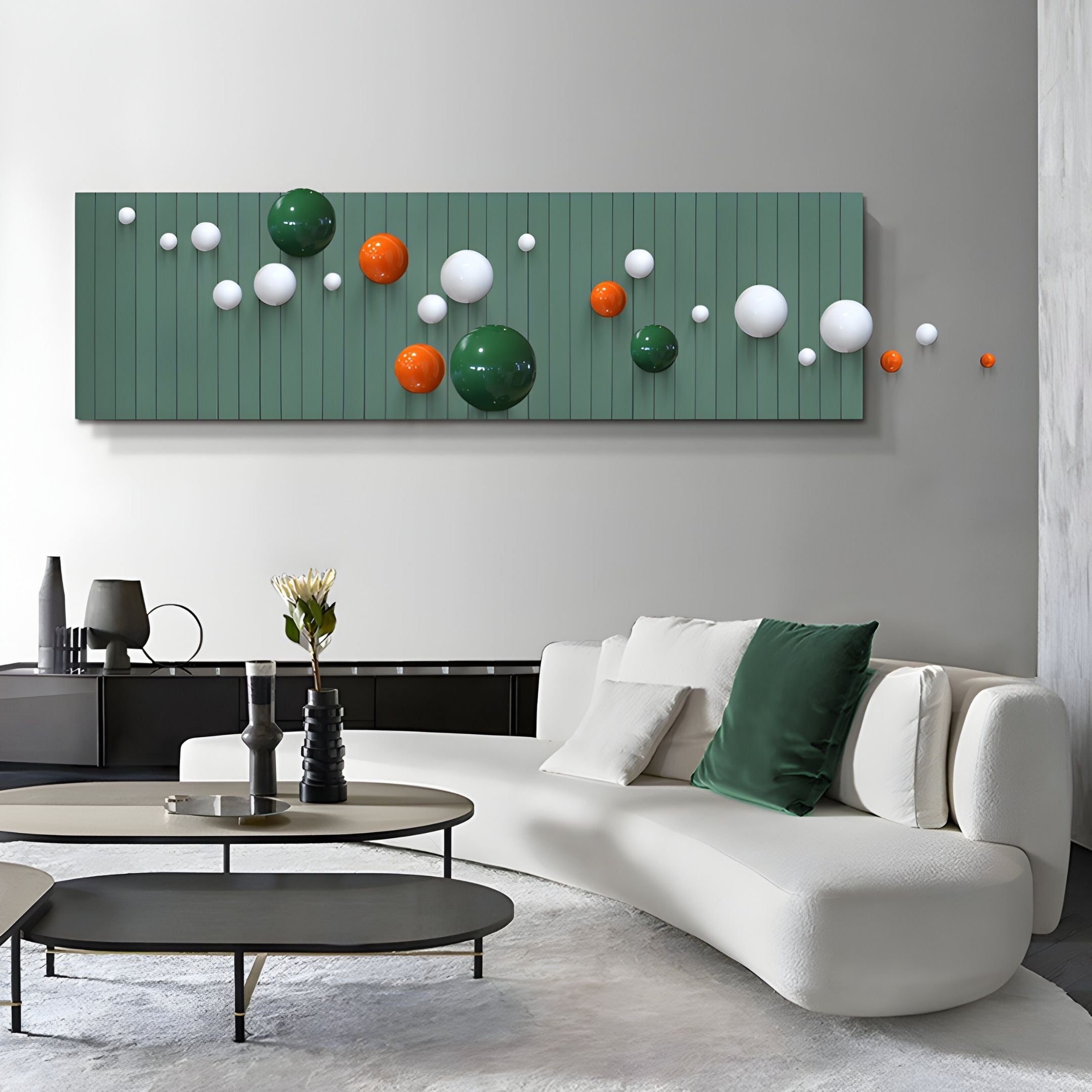 A modern living room features a white sofa with green and white cushions, a minimalist coffee table, and Giant Sculptures' Orbivance Green, White & Orange Sphere Panel 3D Wall Art. Vases and a flower add the finishing touch to the table.