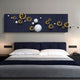 A modern bedroom features a dark blue bed with white bedding and Giant Sculptures’ Orbivance Navy, Gold & White Sphere Panel 3D Wall Art above the bed. Nightstands with lamps are placed on either side.