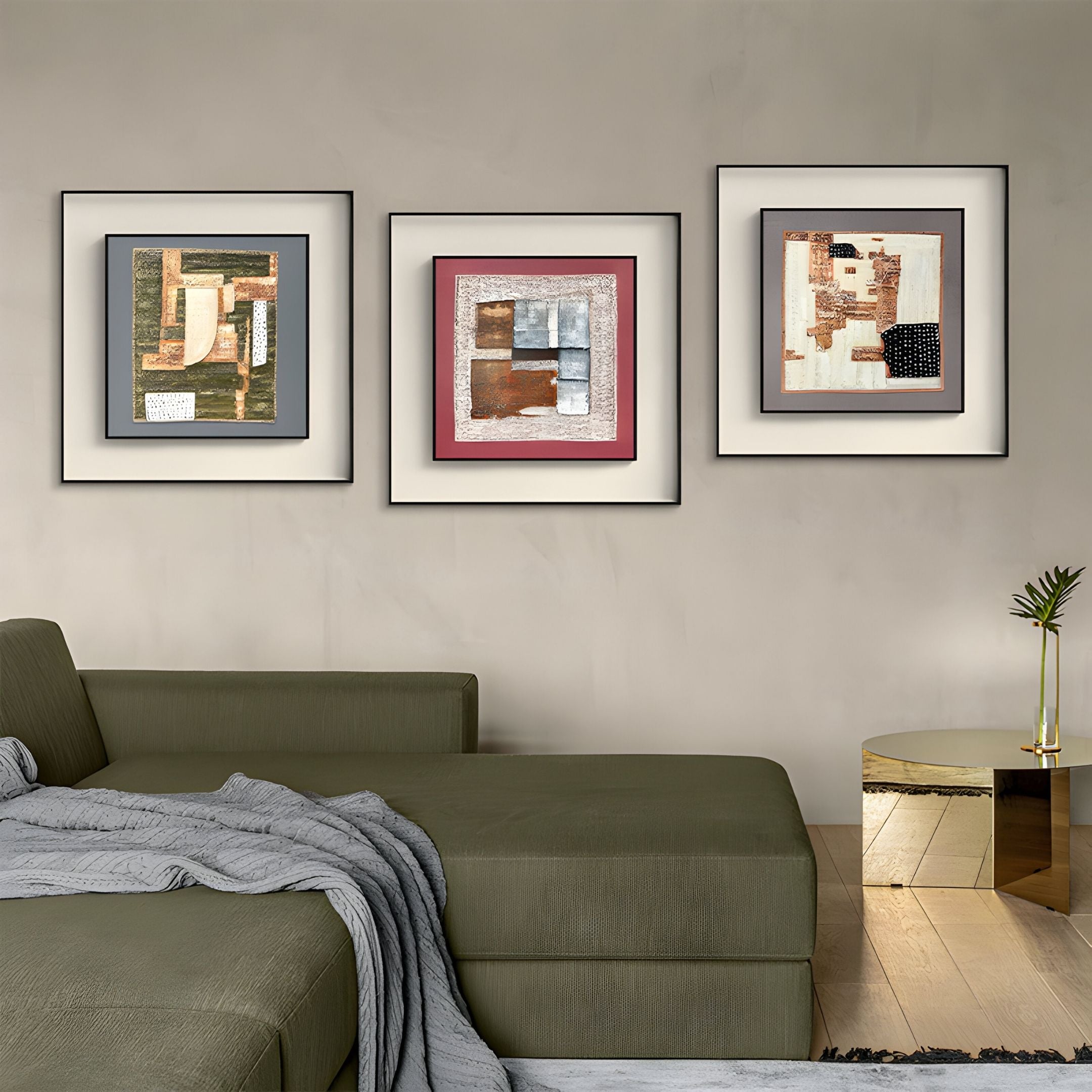A modern living room featuring a green sectional sofa, a gray blanket, a round gold side table with a vase, and three Terralume Rustic Olive & Sand Textured Framed Wall Art pieces by Giant Sculptures on a beige wall.