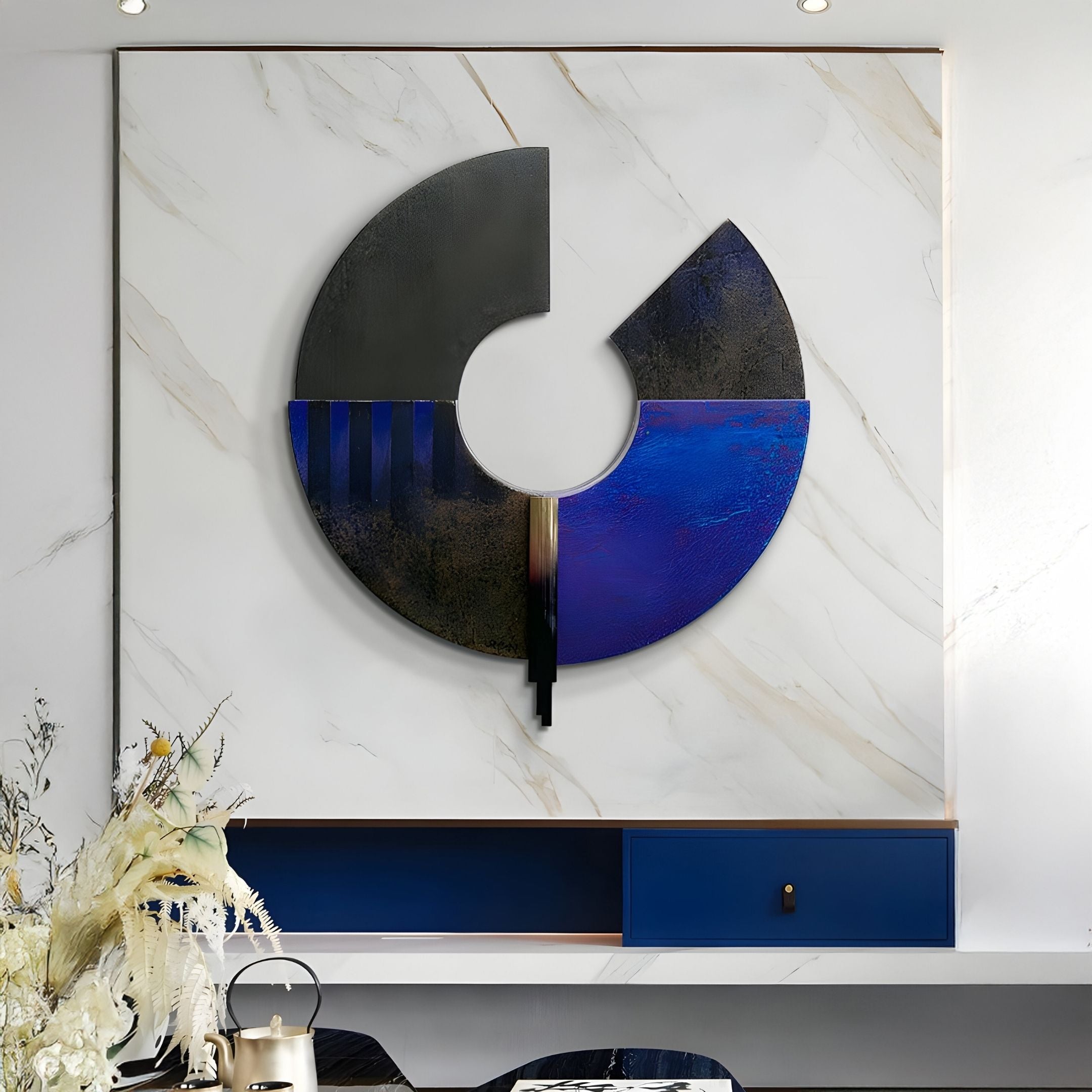 The Vortaryn Midnight Blue & Grey Circle Sculptural 3D Wall Art by Giant Sculptures, featuring a bold circular design with a missing segment, is mounted on white marble above a blue shelf with dried flowers and a metallic teapot in front.