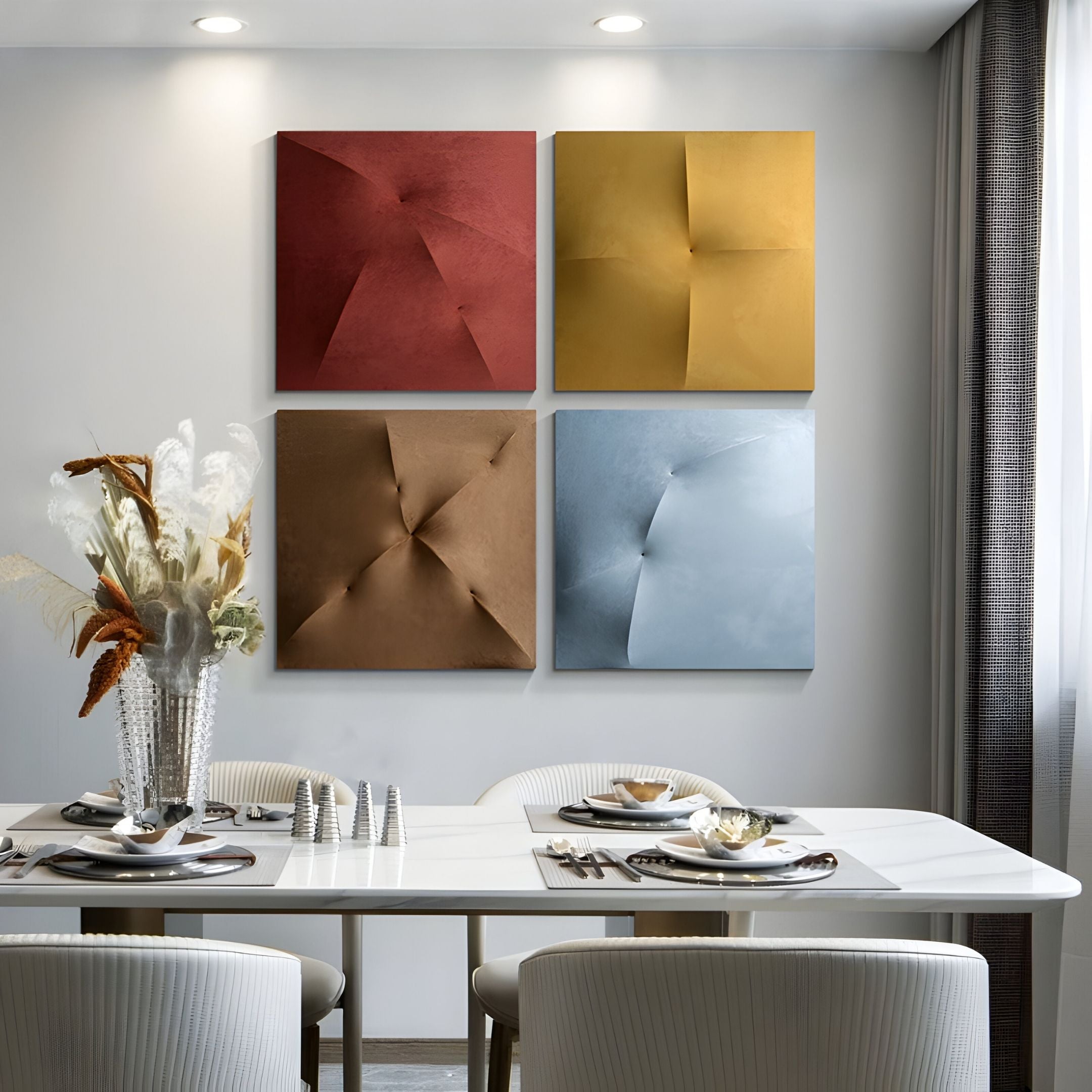 A modern dining room features a white table set for four, white chairs, a vase of dried flowers, and four Giant Sculptures Veylora Terra Folded Texture Fabric 3D Wall Art pieces in red, yellow, bronze, and blue on a crisp white wall.