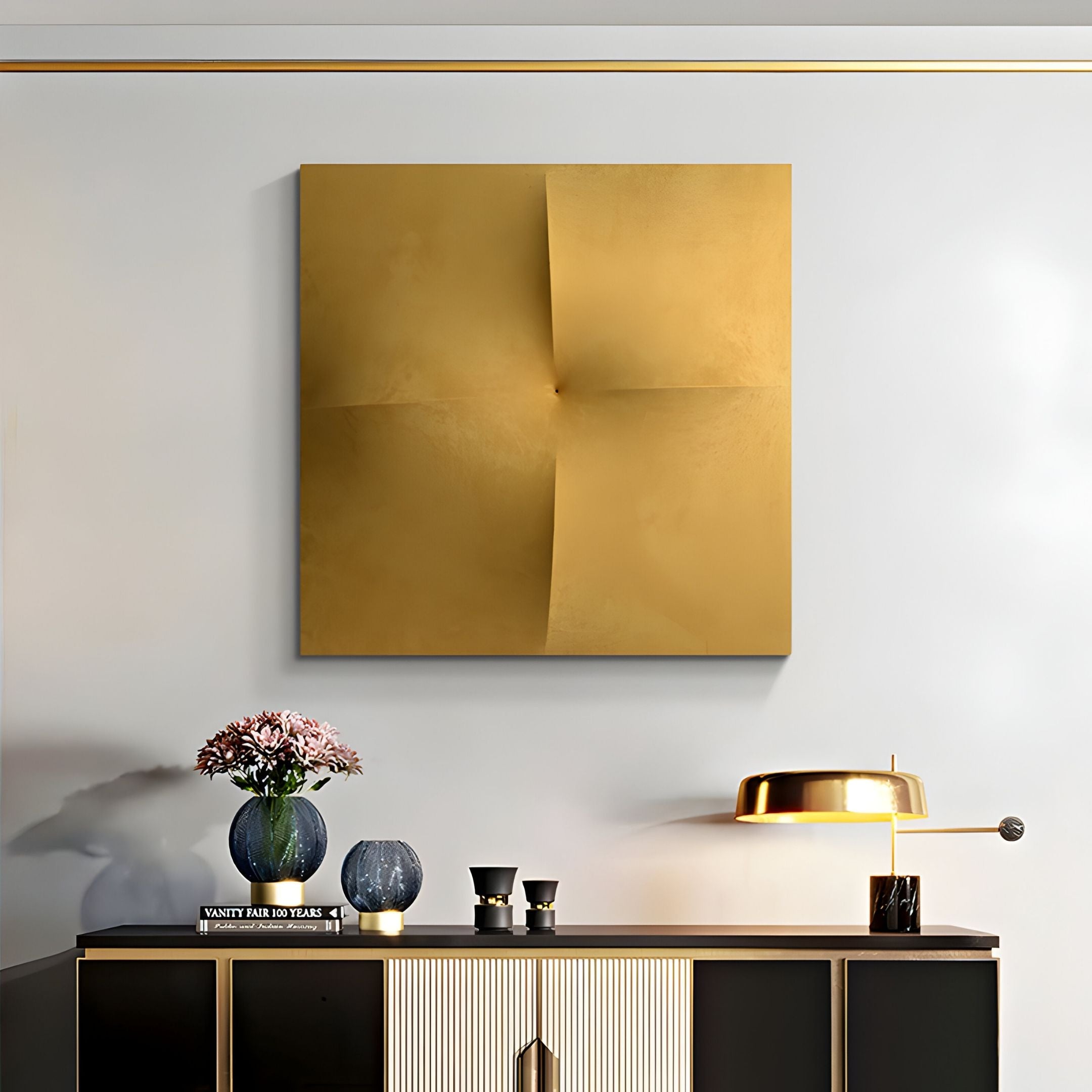 A modern living room featuring the Veylora Gold Folded Texture Fabric 3D Wall Art by Giant Sculptures, a black and gold console table, a vase of pink flowers, books, two small cups, and a gold desk lamp.