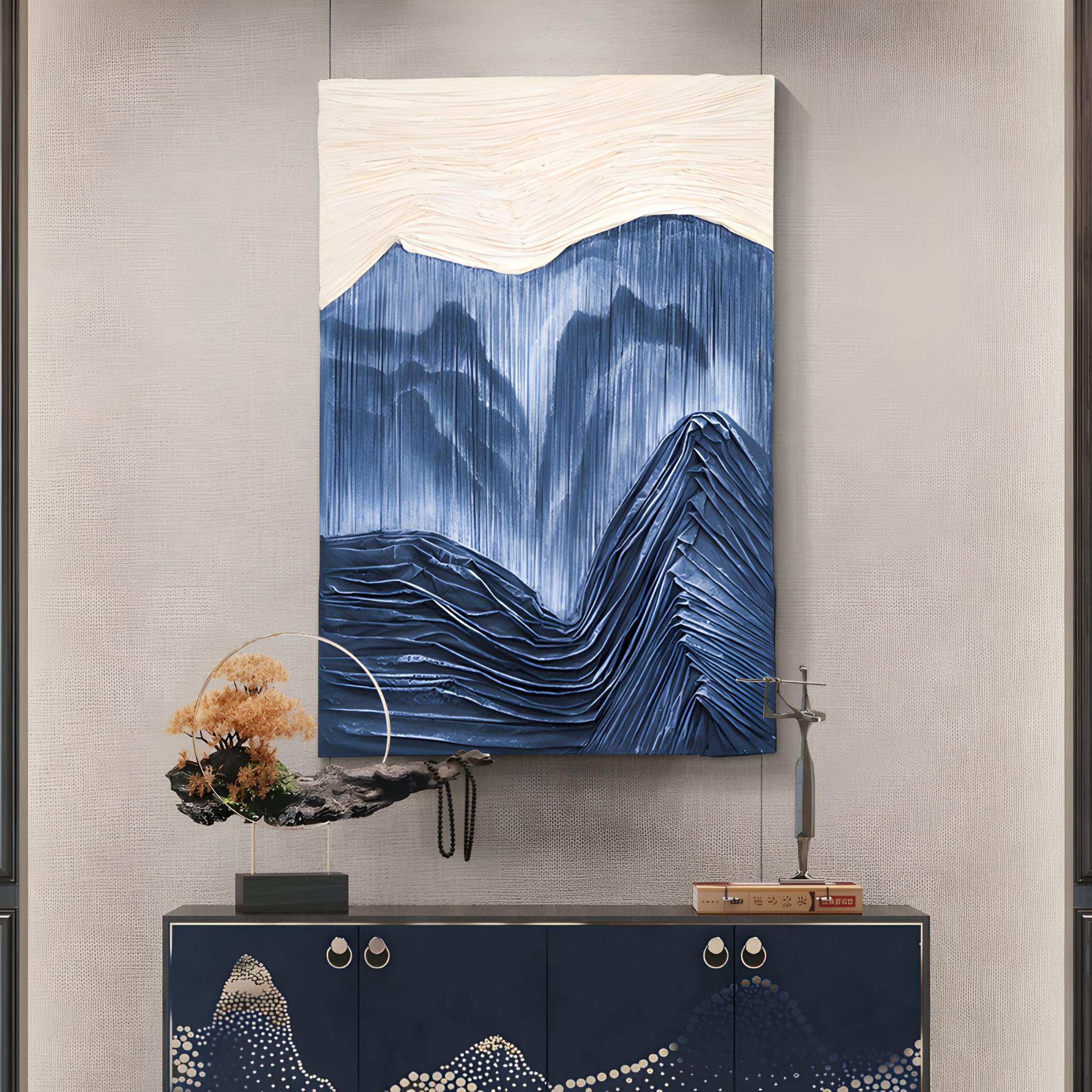 The Terralune Blue Layered Ridge 3D Wall Art by Giant Sculptures hangs above a dark console table, which is decorated with a bonsai tree in a glass display and a small stack of books against a neutral wall.