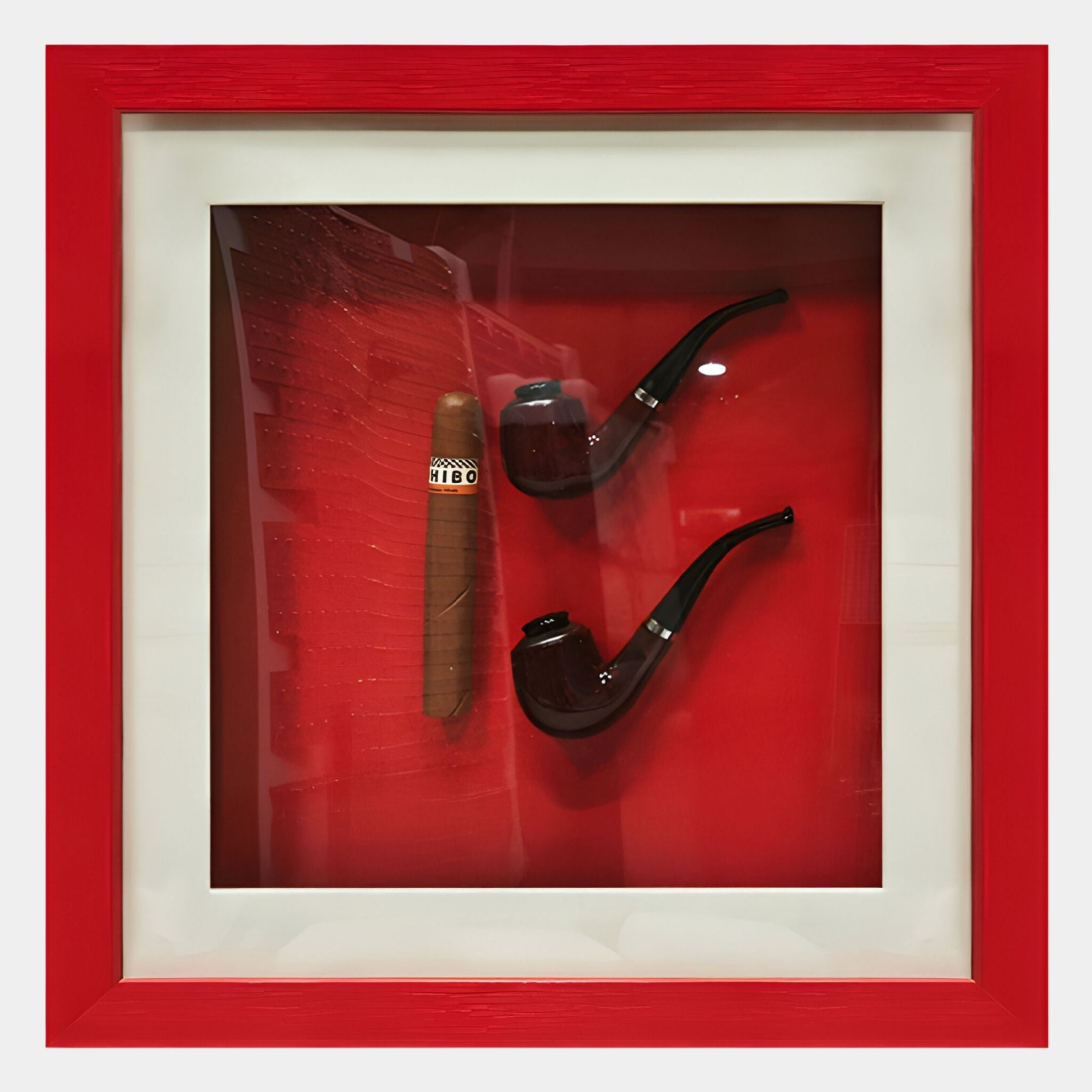 The Cavendro Twin Pipes & Cigar Framed Wall Art by Giant Sculptures showcases a single cigar and two curved pipes arranged vertically on a vivid red background, set within a white mat and red frame.