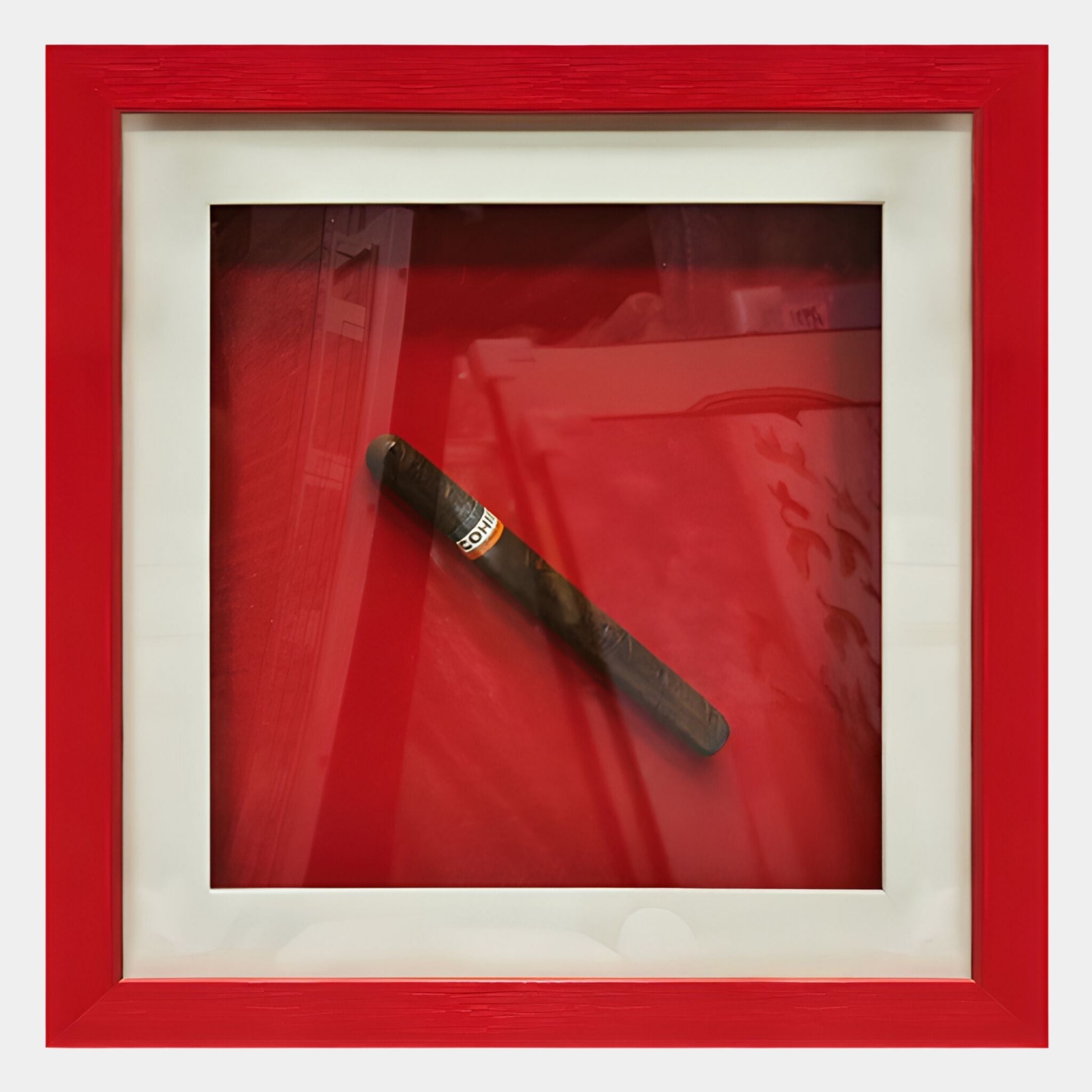 The Cavendro Single Dark Cigar Framed Wall Art by Giant Sculptures features a dark cigar with a gold and red band, set diagonally in a white mat and red frame—perfect as bold accent decor or modern wall art for any space.