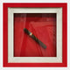 The Cavendro Single Dark Cigar Framed Wall Art by Giant Sculptures features a dark cigar with a gold and red band, set diagonally in a white mat and red frame—perfect as bold accent decor or modern wall art for any space.
