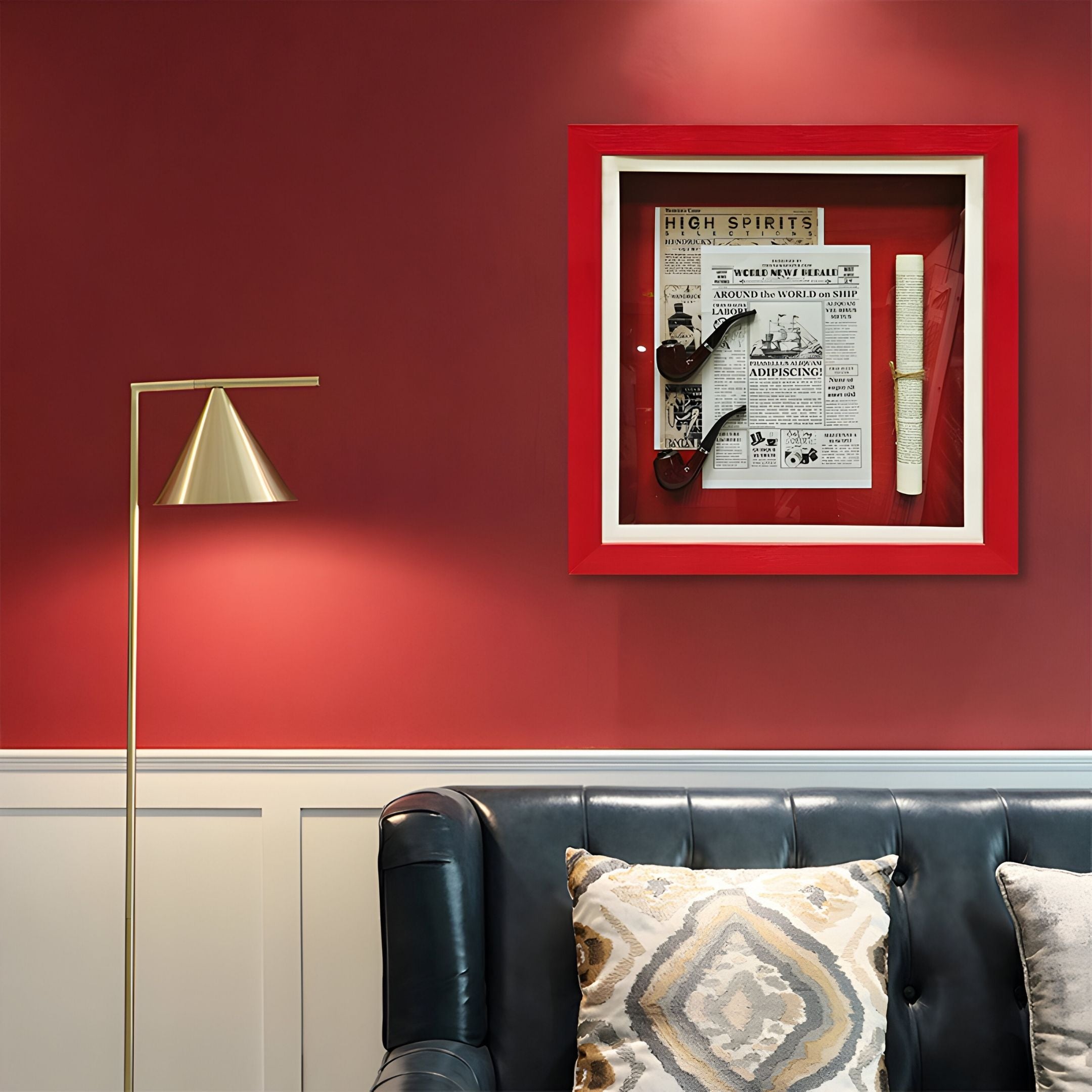 A modern living room with red walls features a black leather couch, patterned pillows, a gold floor lamp, and Giant Sculptures’ Cavendro Newspaper & Pipe Framed Wall Art displayed above the couch for a vintage-inspired touch.