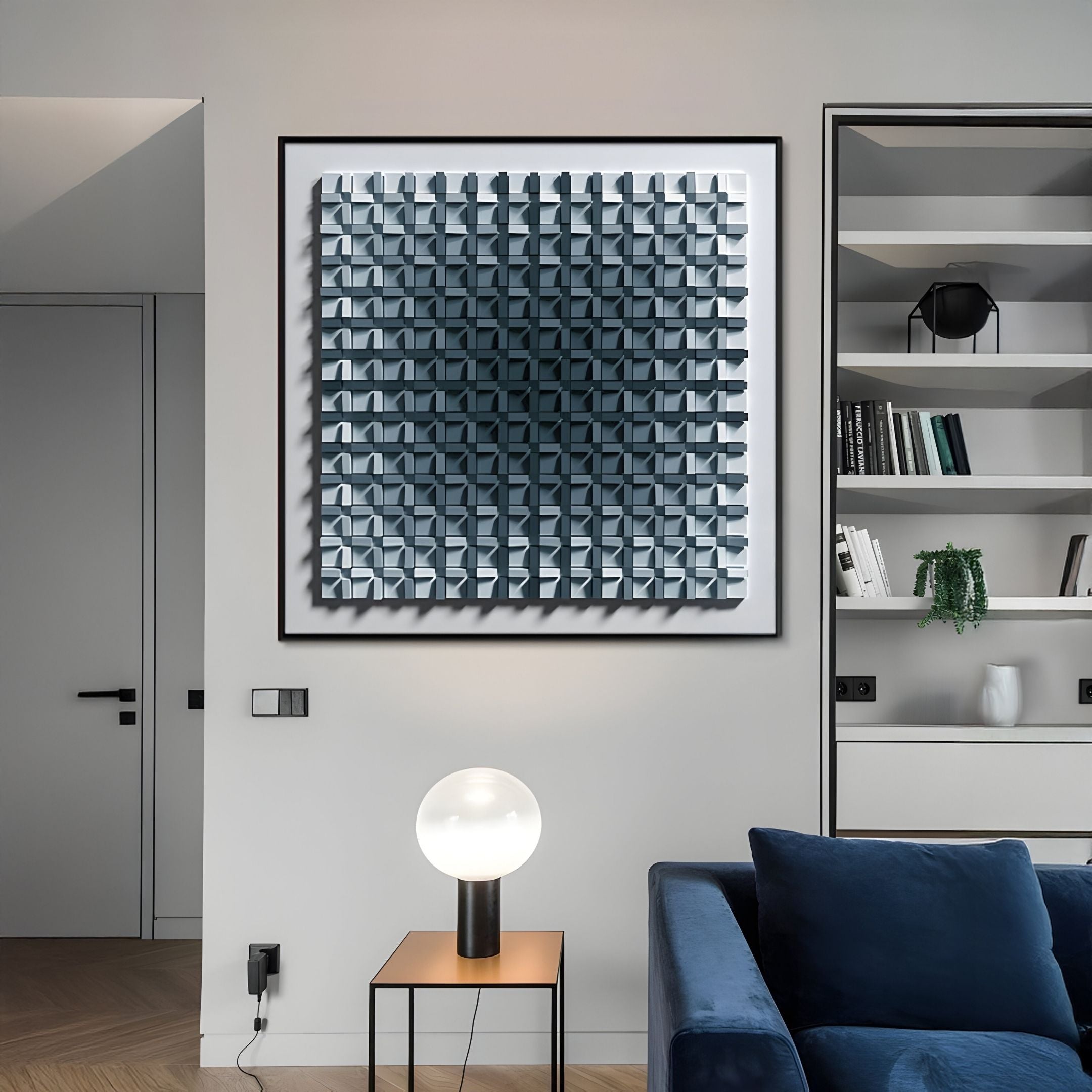 A modern living room features a blue velvet sofa, a round white table lamp on a side table, built-in shelves with books and decor, and the Gradisect Steel Blue Fade Geometric 3D Wooden Wall Art by Giant Sculptures as the striking focal point.