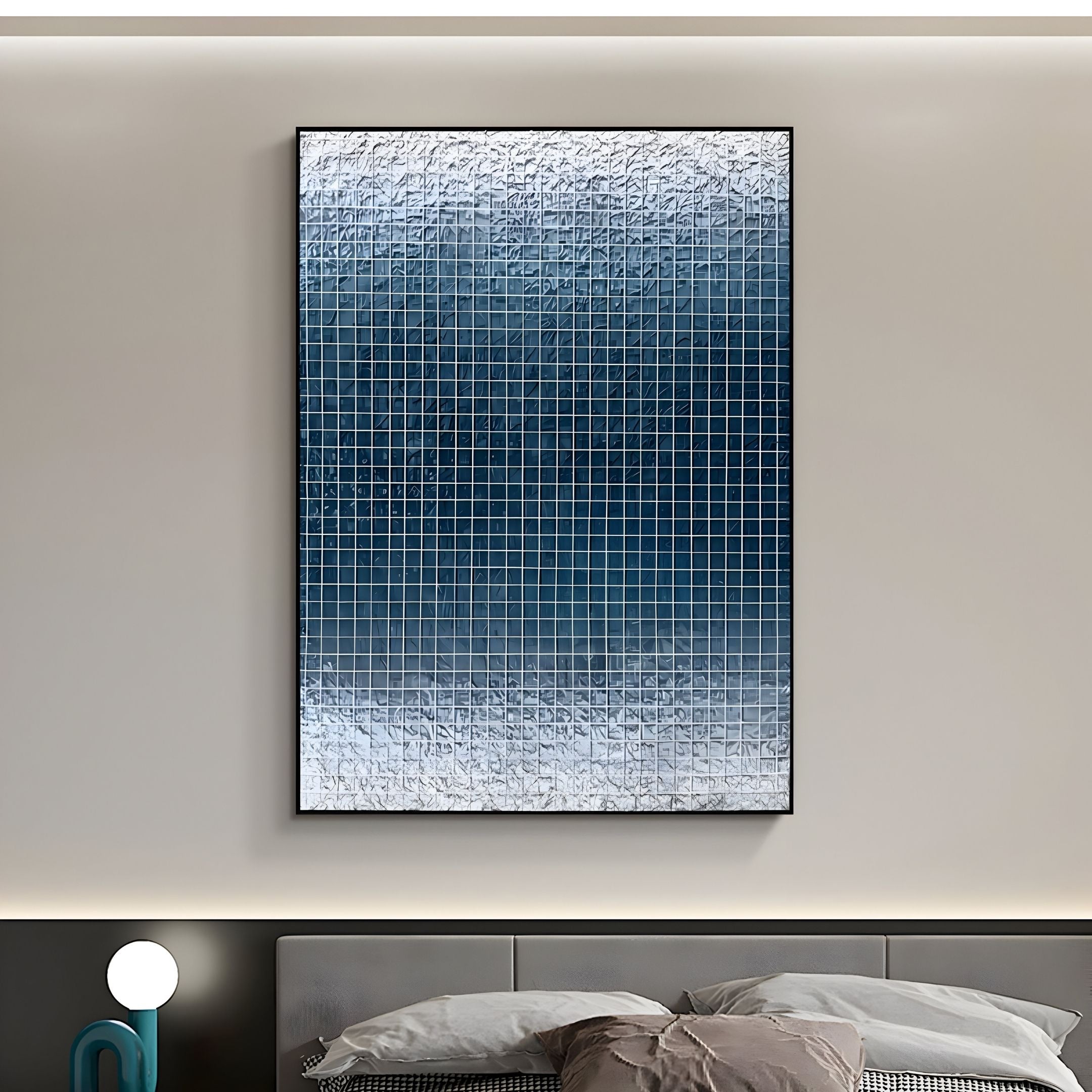 The Gridelle Deep Blue Gradient Grid 3D Paper Wall Art by Giant Sculptures hangs on a beige wall above a bed with gray and beige pillows. A small round lamp is on the bedside table to the left.