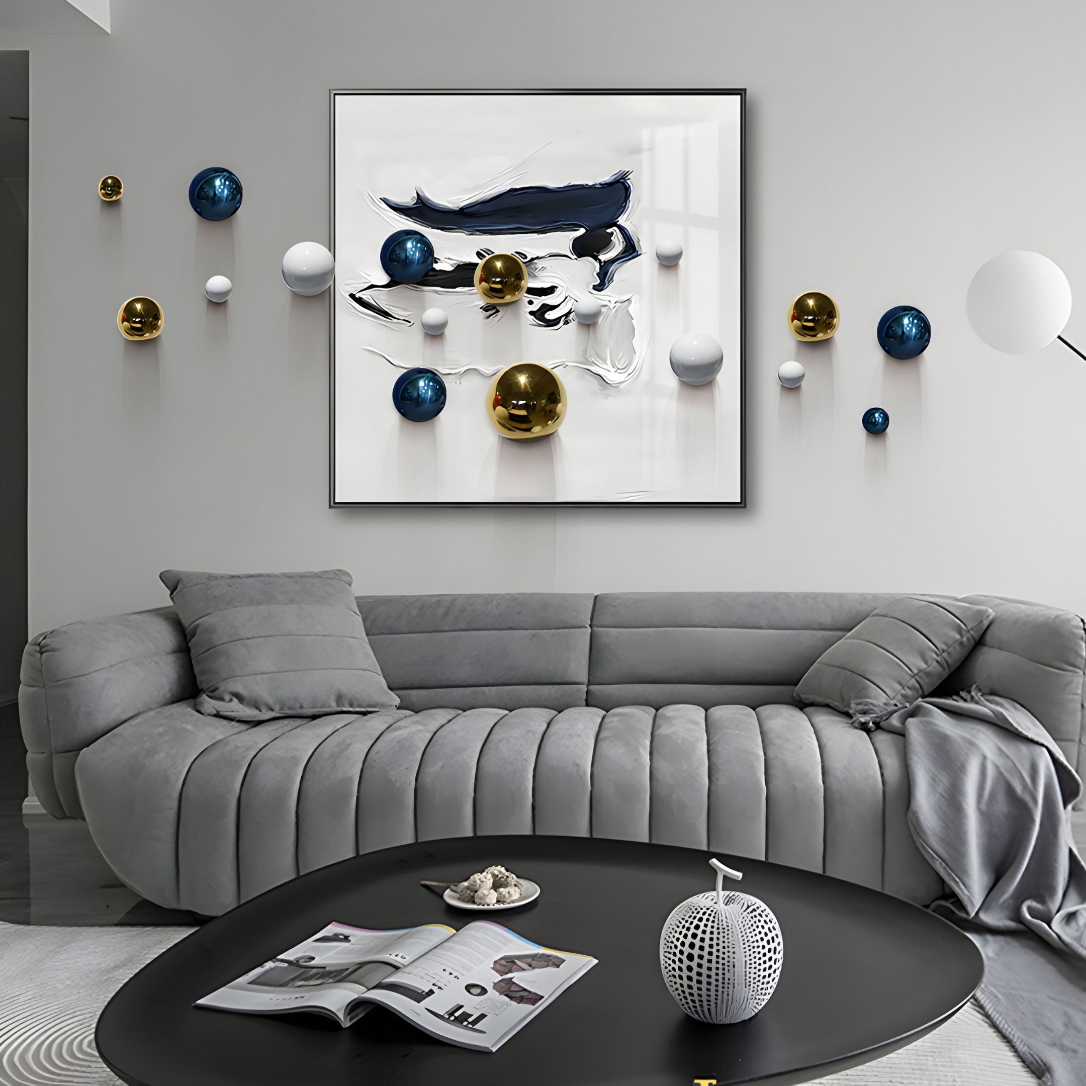 A modern living room with a curved gray sofa, a black oval coffee table with decor and magazines, and Giant Sculptures' Aeroluxe Navy Crest Abstract 3D Wall Art With Metal Balls—ideal for stylish modern interiors.
