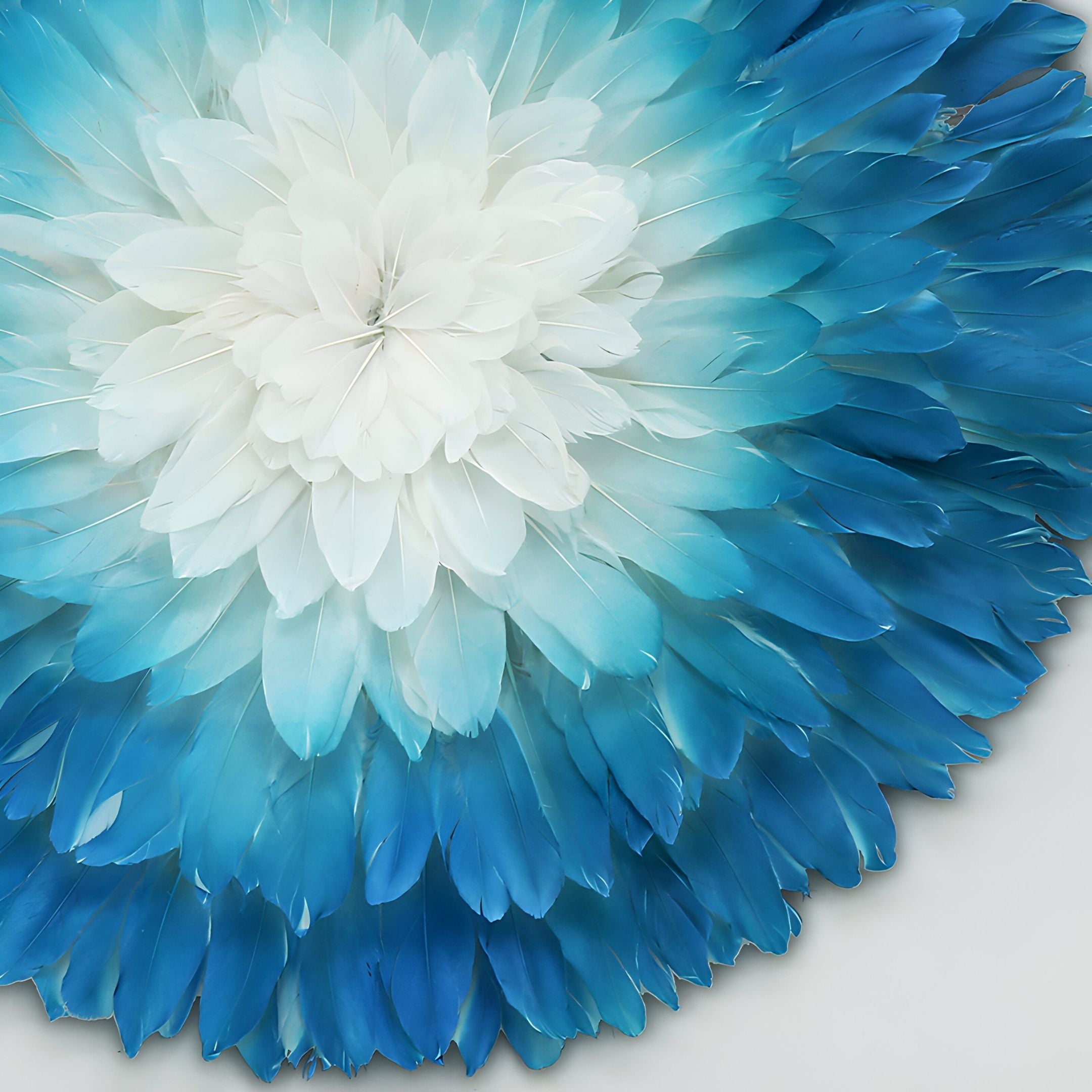 The Plumesse Aqua Bloom Layered Feather 3D Wall Art by Giant Sculptures features circular layers of feathers in white, light, and deep blue, forming a flower-like mandala that stands out on a neutral background.