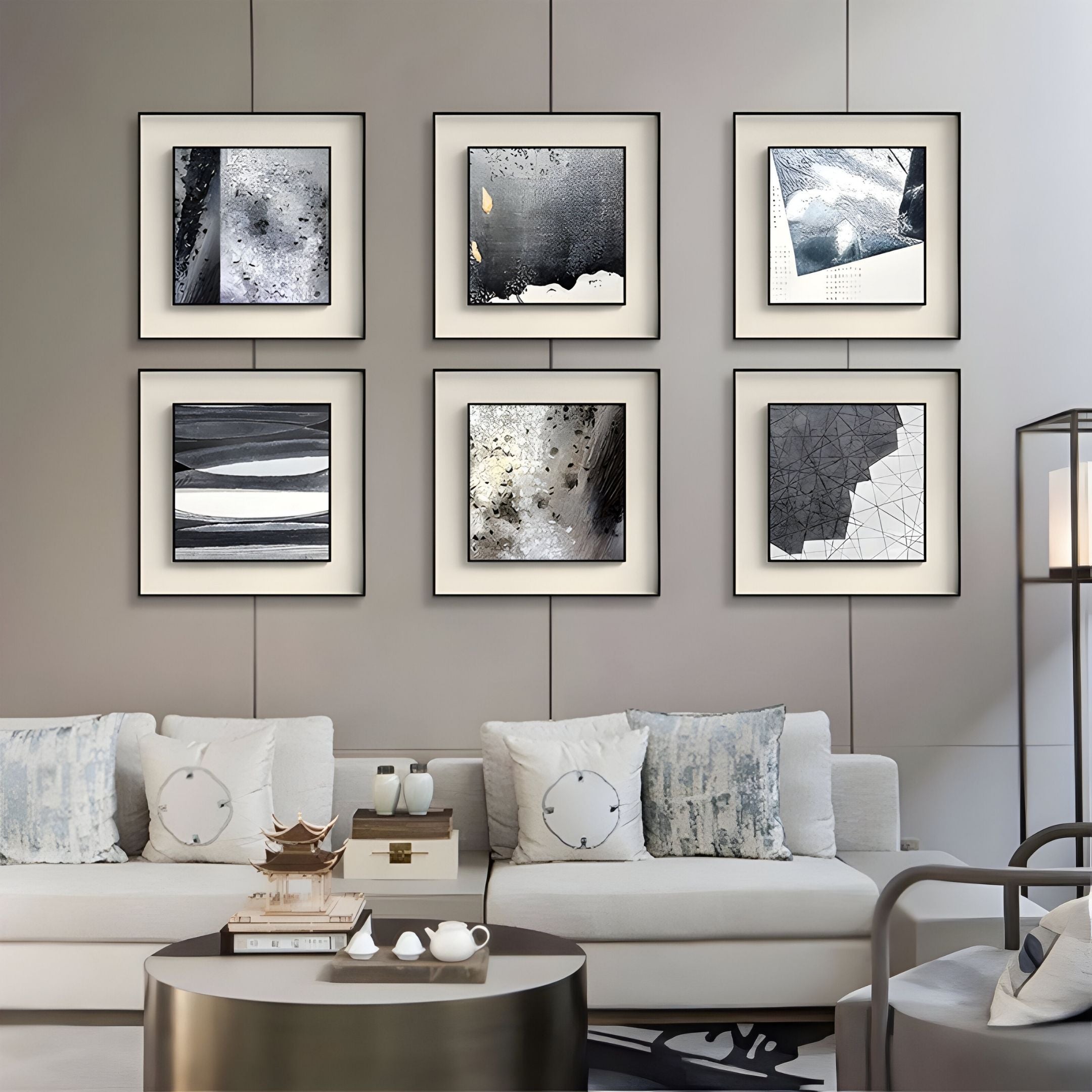 A modern living room with white sofas, patterned pillows, a coffee table, and six Stratonis Graphite Linework Textured Framed Wall Art pieces by Giant Sculptures in black frames arranged in two rows on a light gray wall.