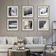 A modern living room with white sofas, patterned pillows, a coffee table, and six Stratonis Graphite Linework Textured Framed Wall Art pieces by Giant Sculptures in black frames arranged in two rows on a light gray wall.