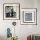 Two Stratonis Grey Linework Textured Framed Wall Art pieces by Giant Sculptures in black frames hang on a light wall above a decorative stand with geometric accents and a green floral arrangement. A beige chair appears in the lower right corner.