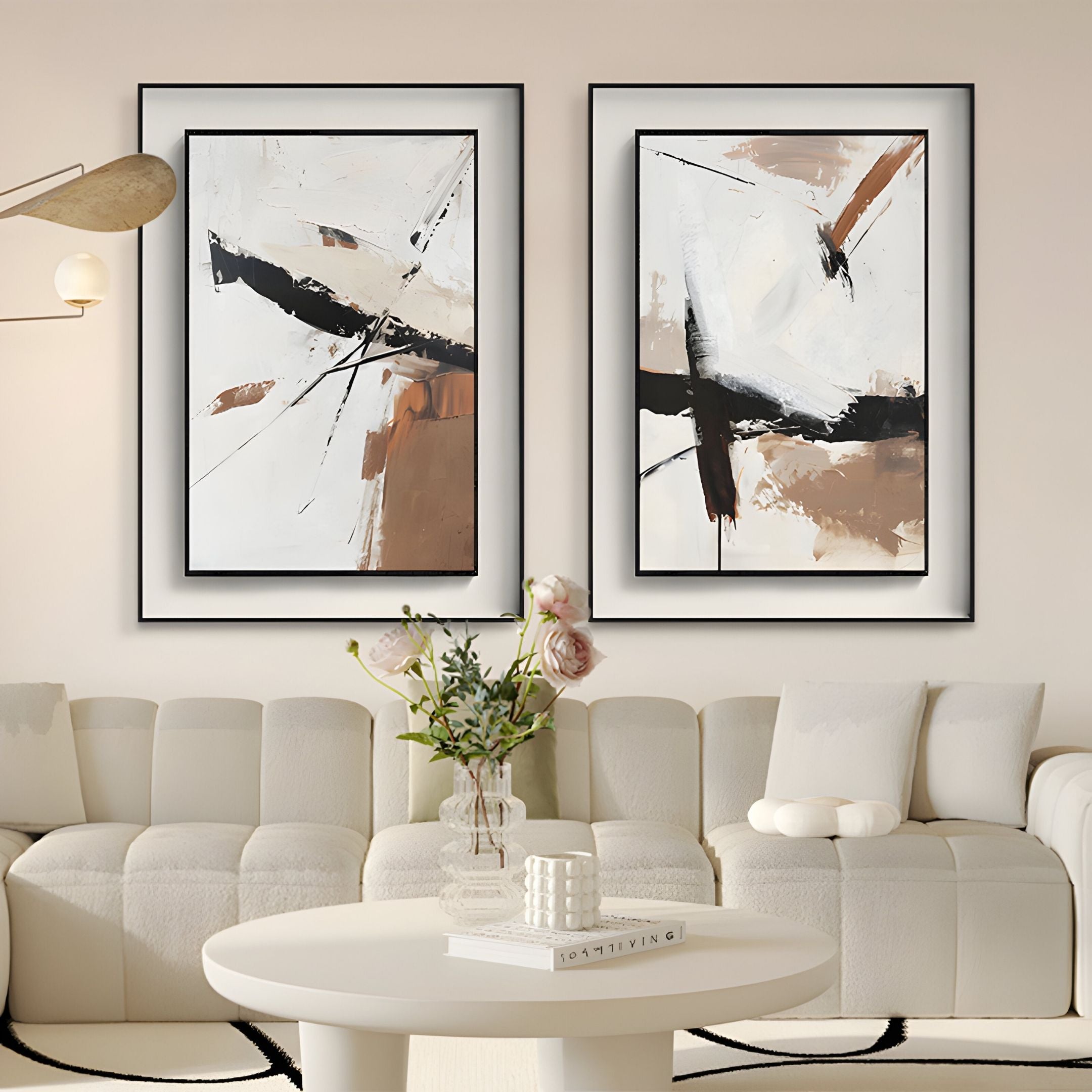 A modern living room with a white sofa, round white coffee table holding a glass vase of flowers, and two Bravura I Stroke Abstract Framed Canvas Wall Art pieces by Giant Sculptures in black frames on the wall.