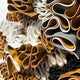 Close-up of Rivora Amber Ribbon Leather Circular 3D Wall Art by Giant Sculptures, featuring rolled and folded sheets in white, brown, tan, and black—an abstract, textured pattern ideal for sculptural wall decor or striking leather wall art.
