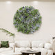 A modern living room showcases the Rivora Green Ribbon Leather Circular 3D Wall Art by Giant Sculptures above a white sofa with cushions, complemented by a small round table and a leafy plant in front.