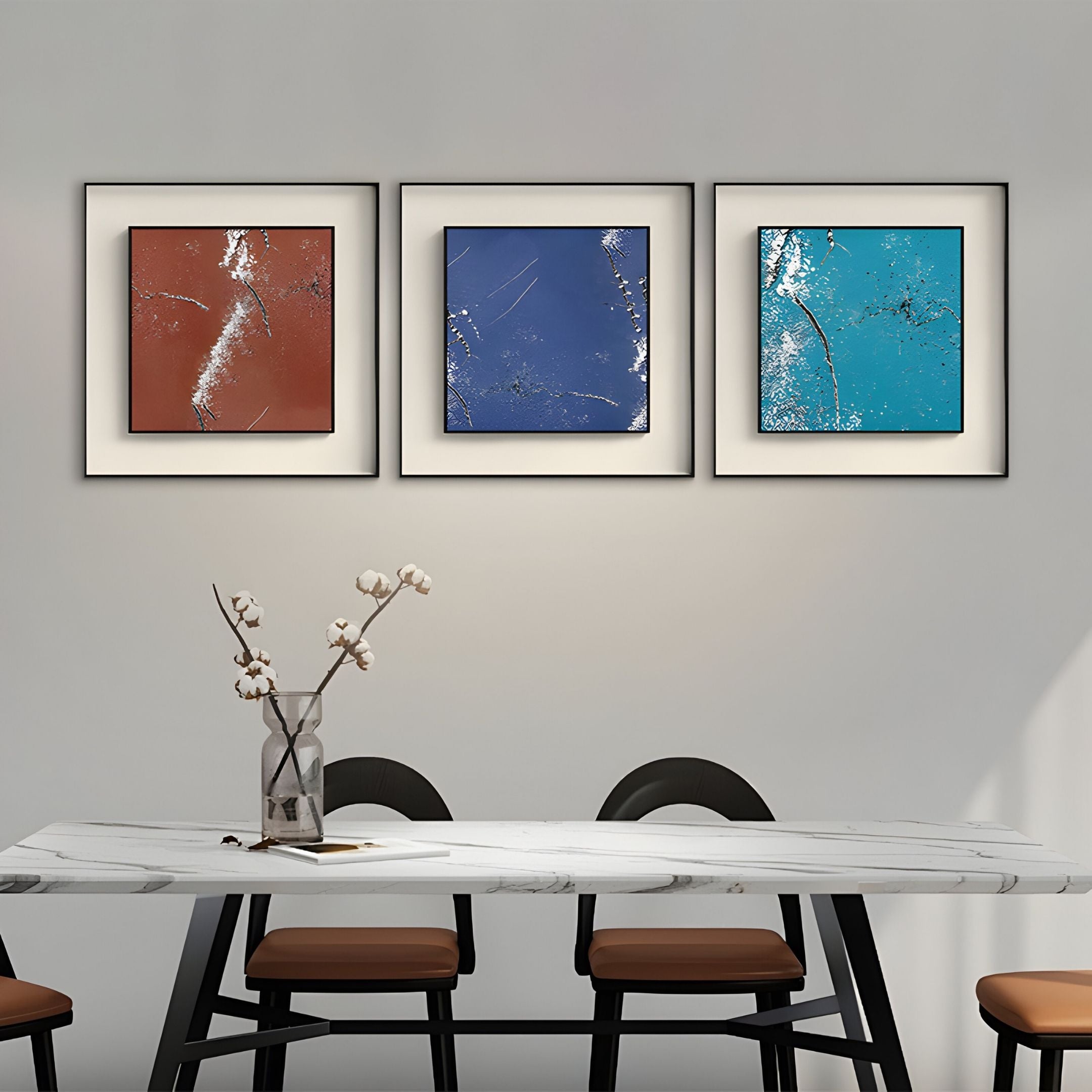 A modern dining area features a marble table, four chairs, and a glass vase with white flowers. Above, three Trevasse Aqua Blue Textured Abstract Framed Wall Art pieces by Giant Sculptures add vibrant color to the light gray wall.